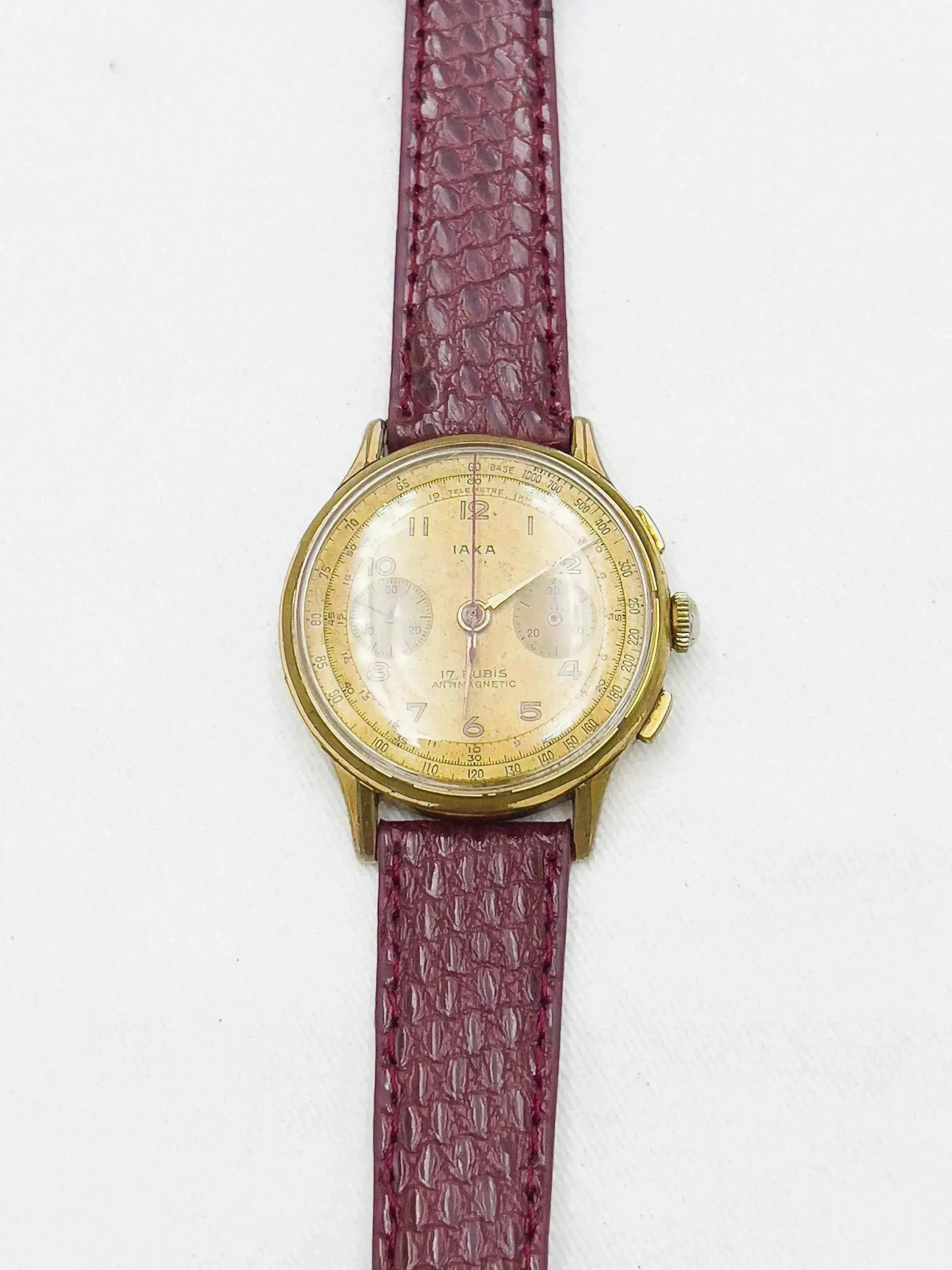 Vintage Iaka chronograph watch with gold case, cream dial, and burgundy leather strap