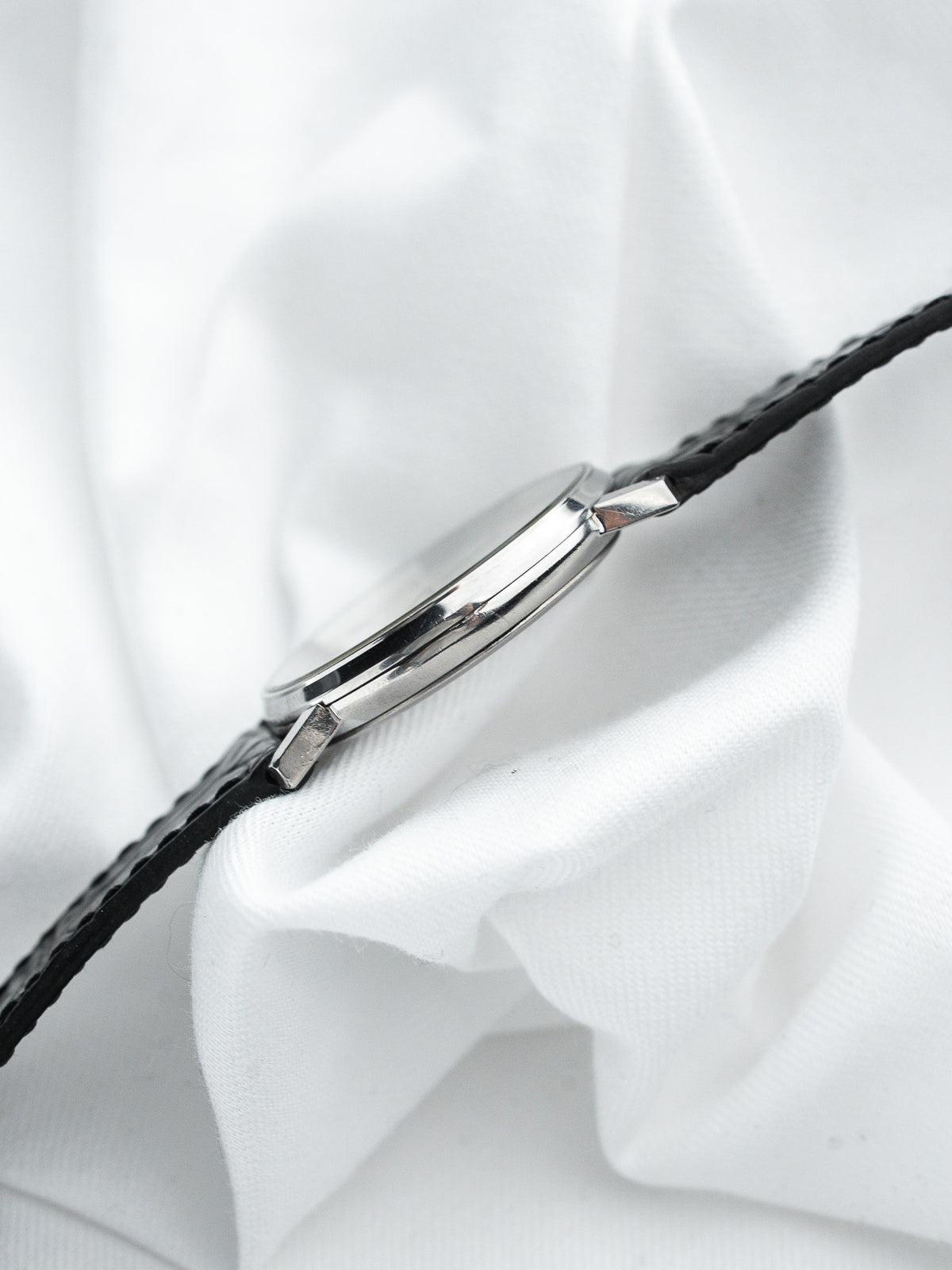 Montre vintage au boîtier argenté et bracelet en cuir noir sur fond blanc