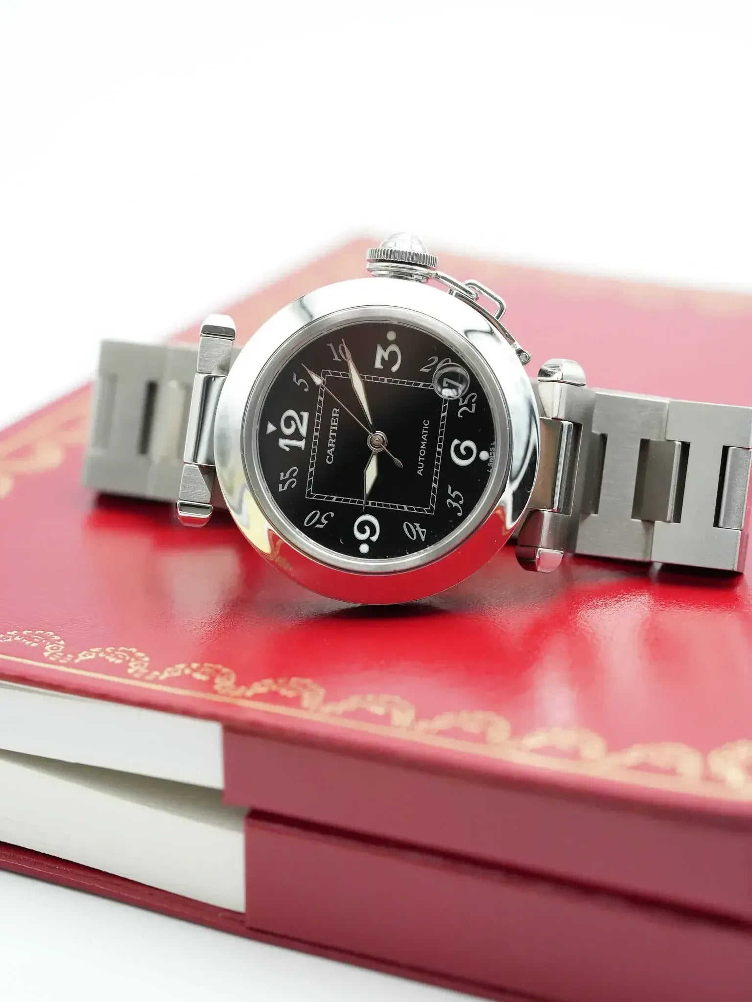Cartier Pasha vintage watch with black dial, steel case, resting on red book