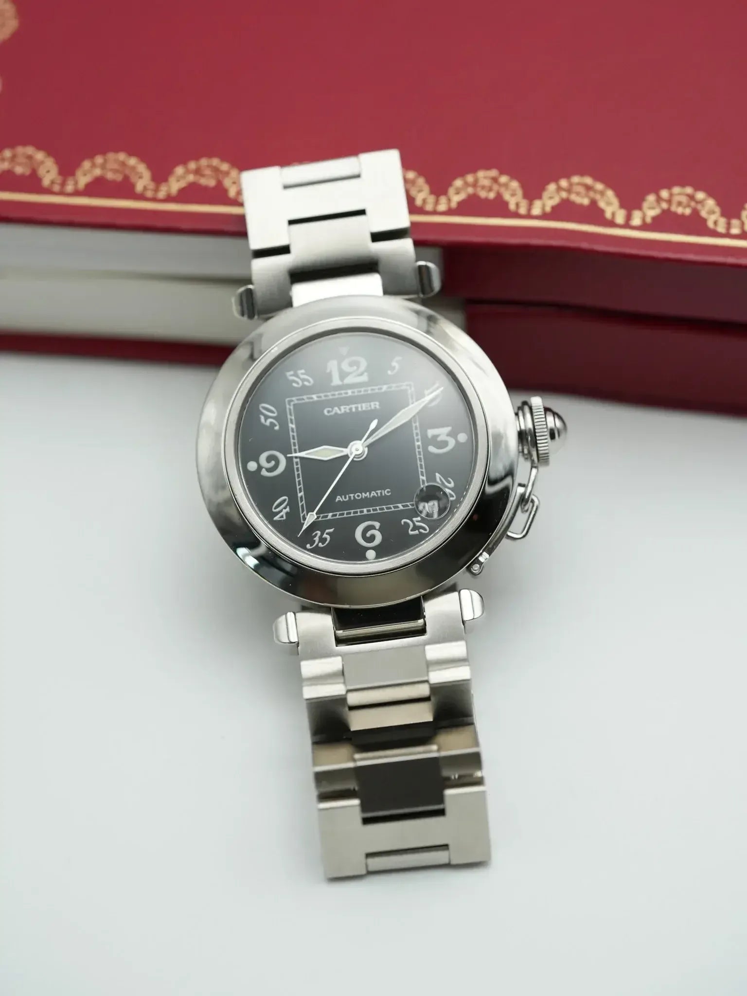 Cartier Pasha automatic watch with black dial and steel bracelet, displayed against red box