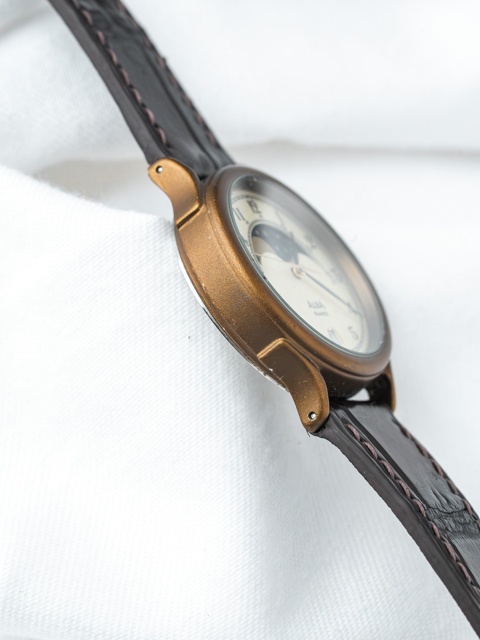 Vintage watch with bronze case, cream dial, black leather strap on white fabric
