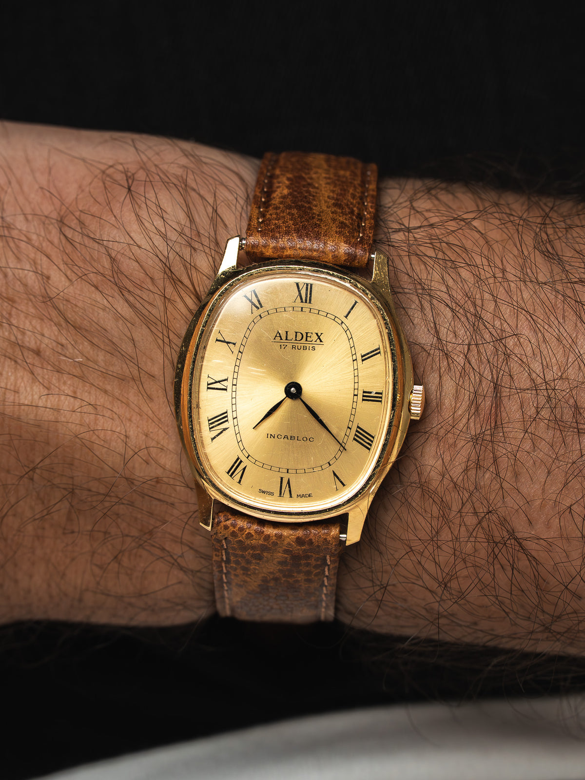 Montre Aldex vintage dorée avec cadran champagne et bracelet cuir marron au poignet