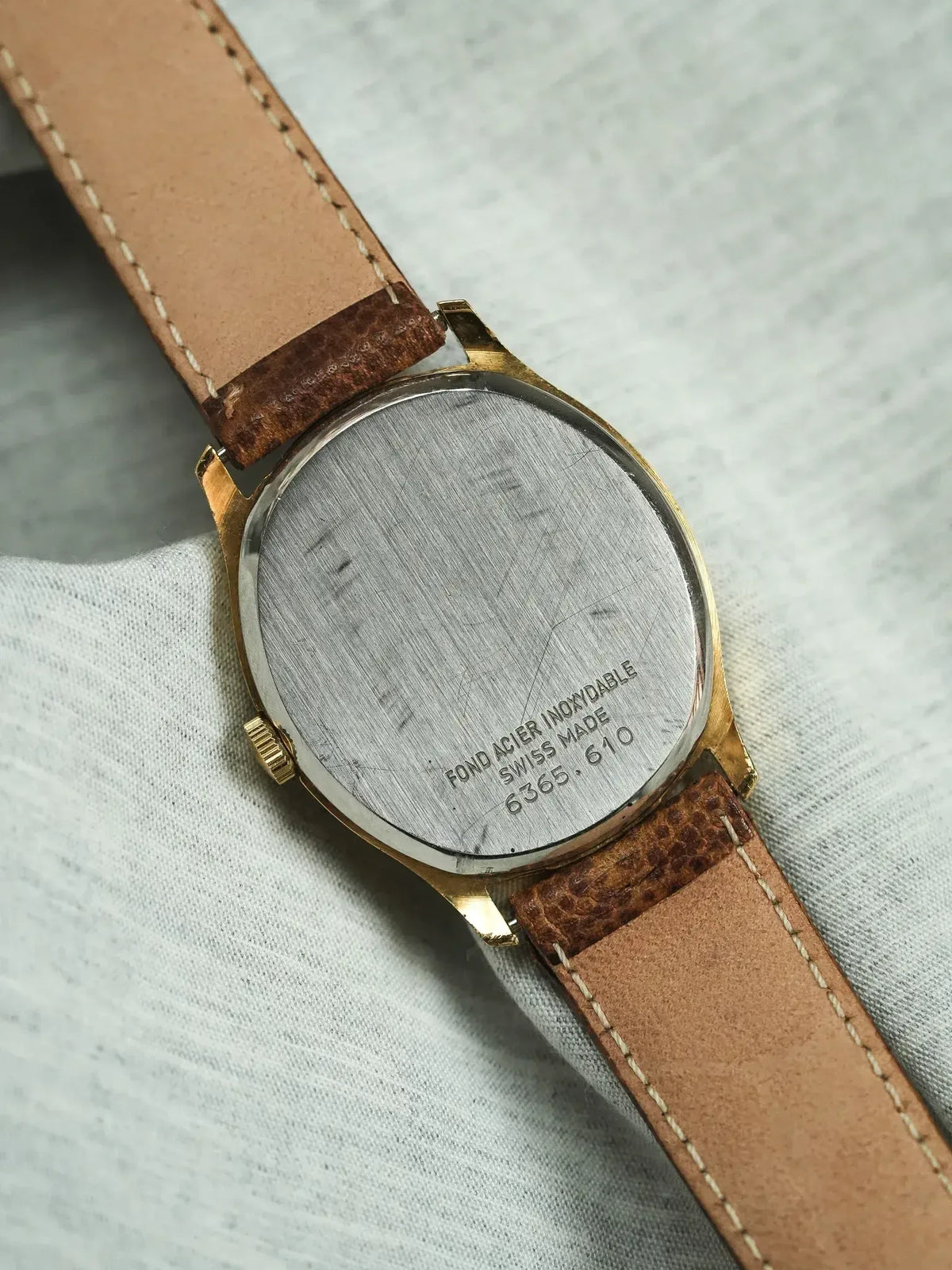 Vintage watch with gold case, stainless steel back, brown leather strap on fabric