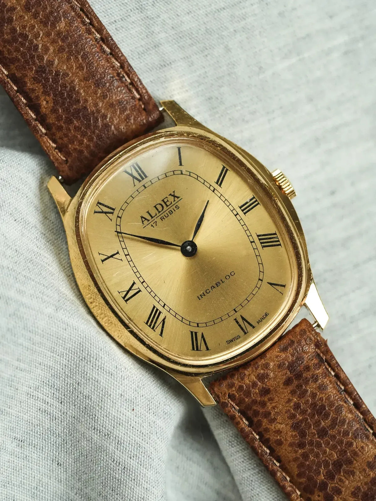 Vintage Aldex watch with gold case, Roman numerals, and brown leather strap