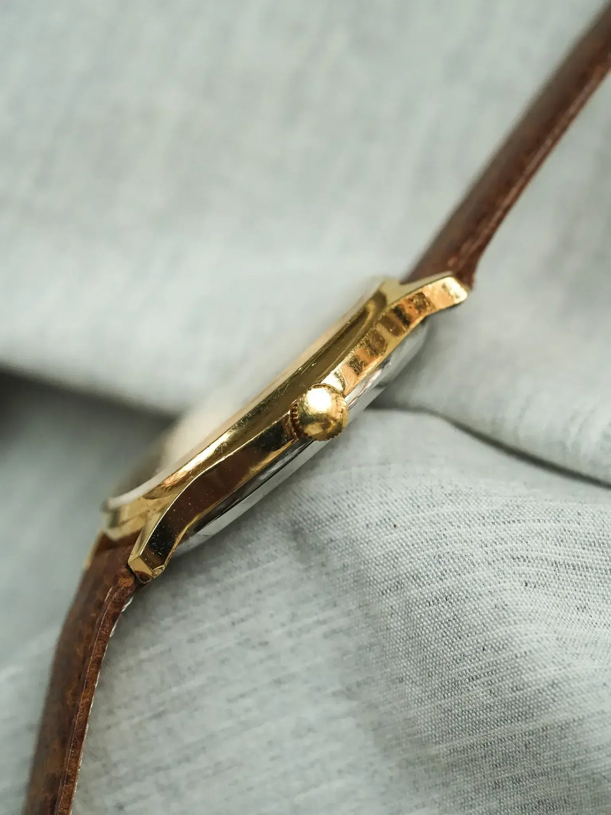 Vintage Rolex watch with gold case and brown leather strap on fabric