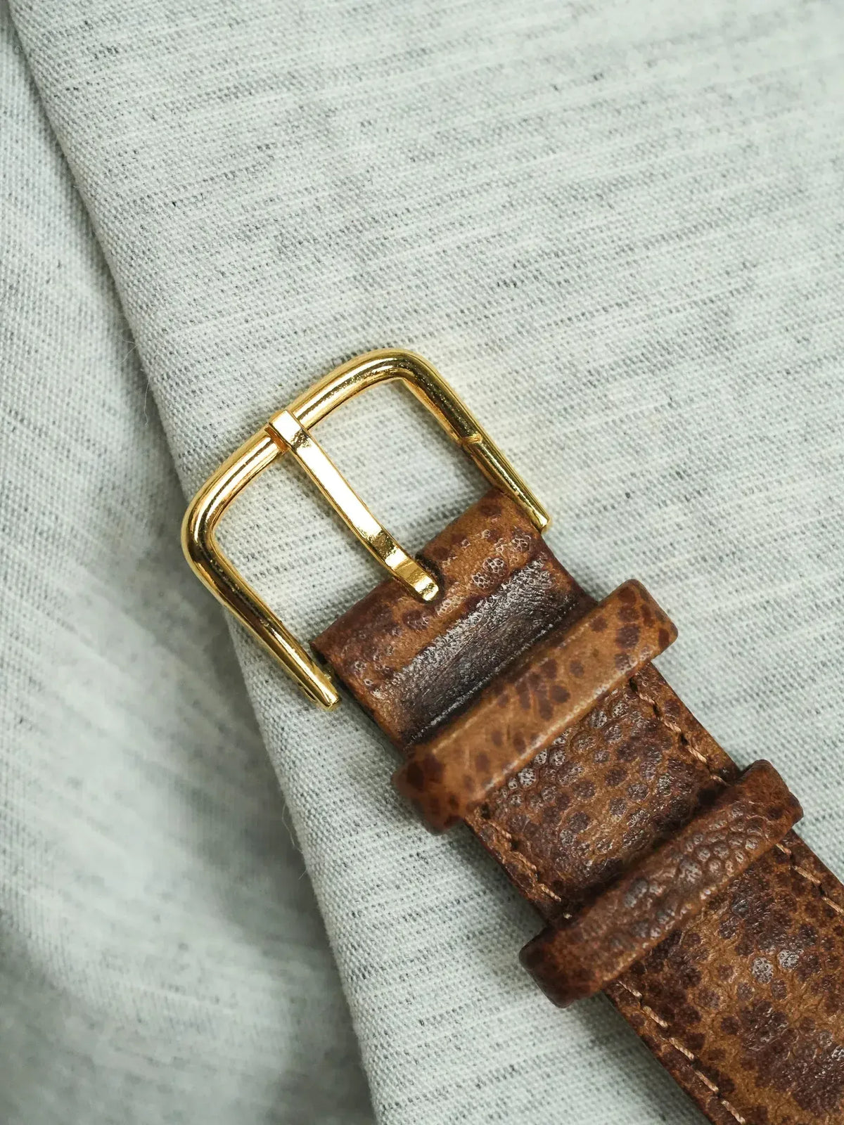 Vintage brown leather watch strap with gold buckle on textured fabric
