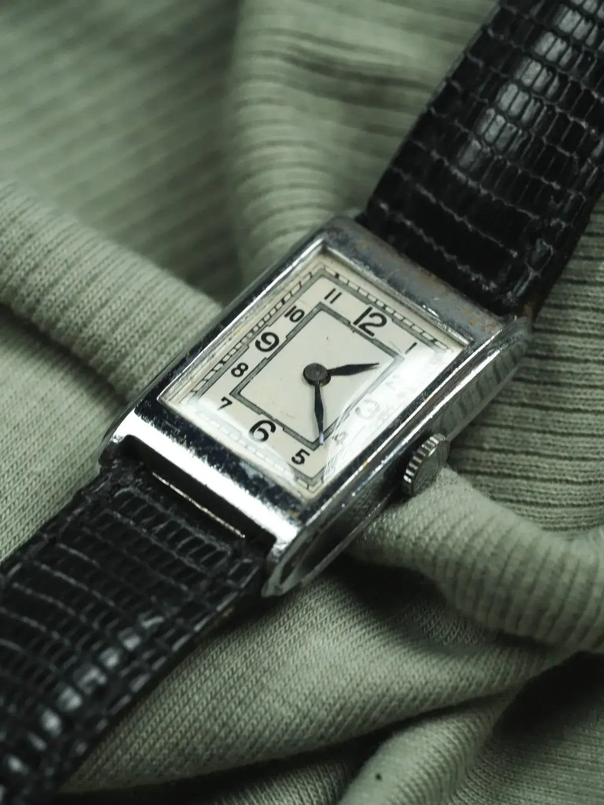 Vintage rectangular watch with silver case, white dial, black leather strap on green fabric