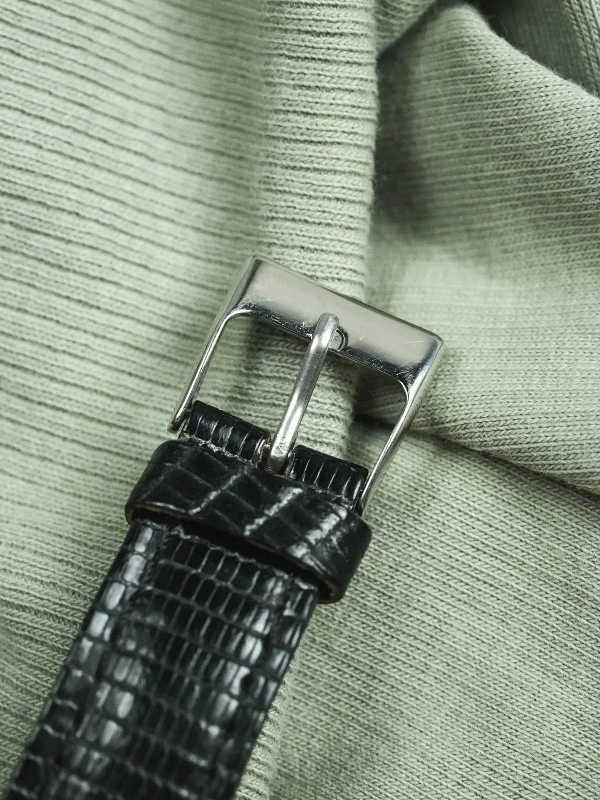 Black alligator leather watch strap with polished steel buckle on green fabric