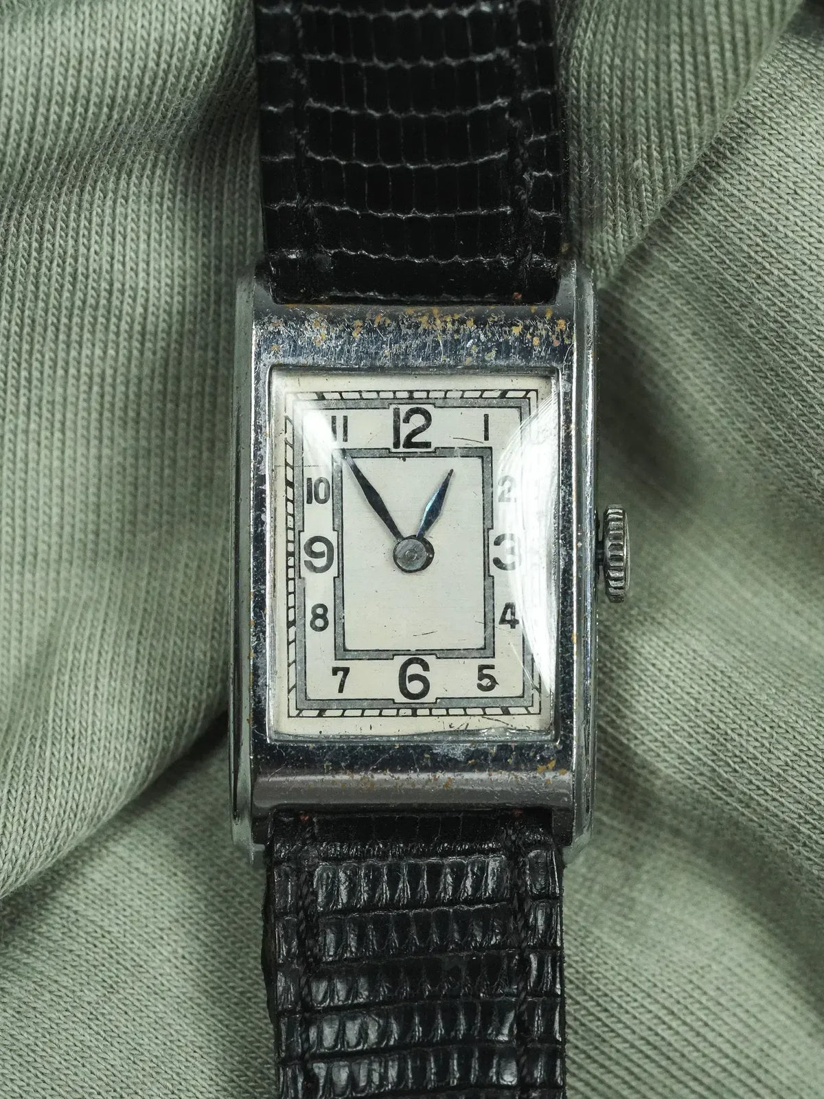 Vintage rectangular watch with white dial, black numerals, and textured black strap on fabric