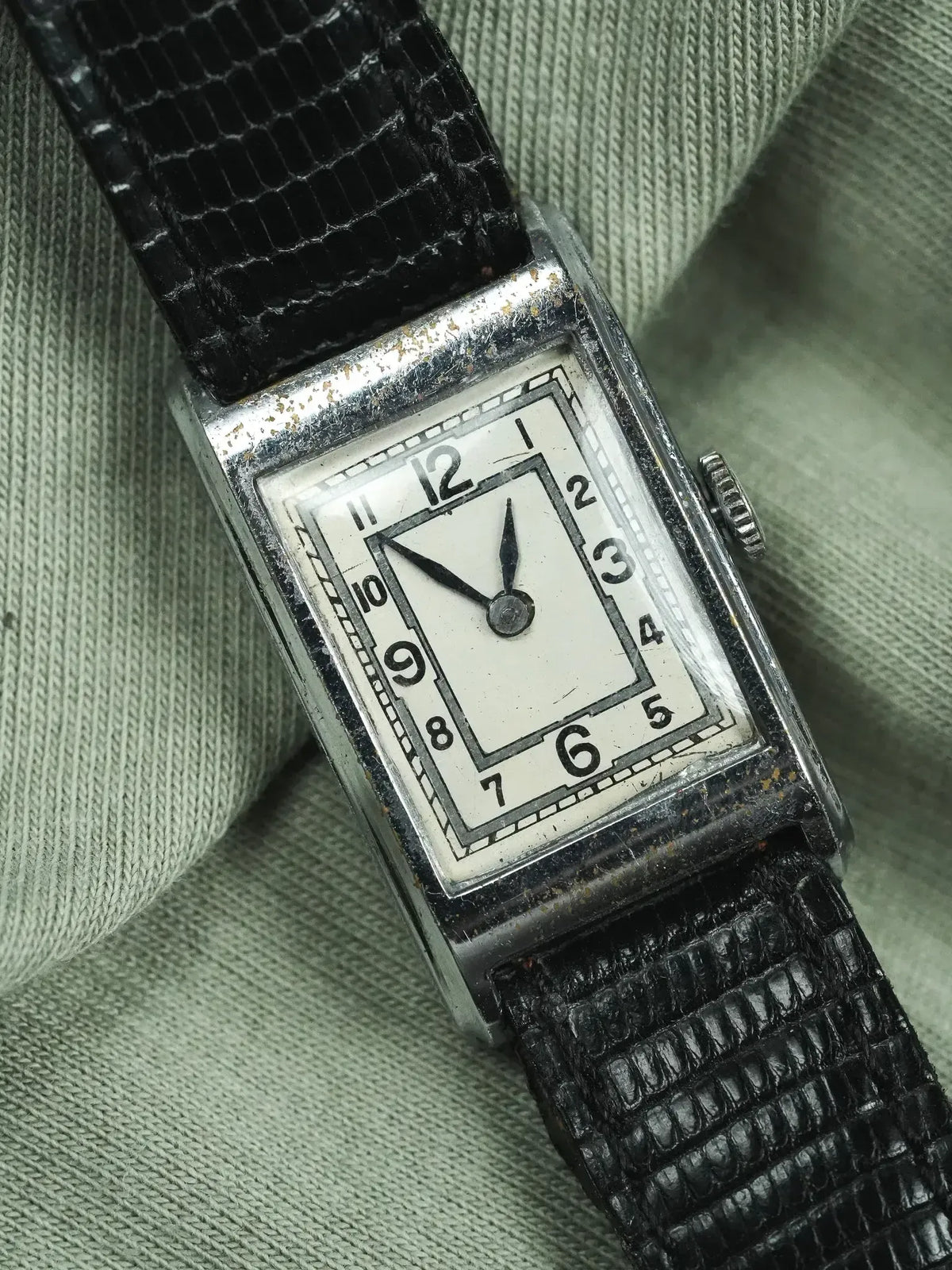 Vintage rectangular watch with white dial, black numerals, and black alligator strap on fabric