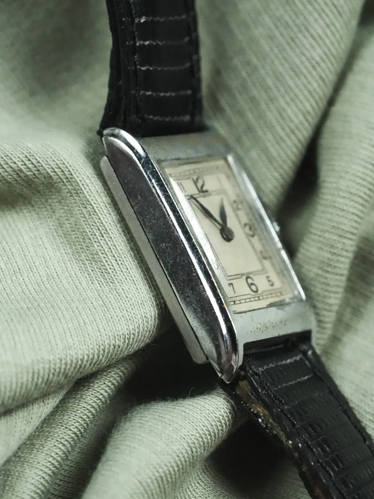 Vintage rectangular watch with silver case, cream dial, black leather strap on fabric