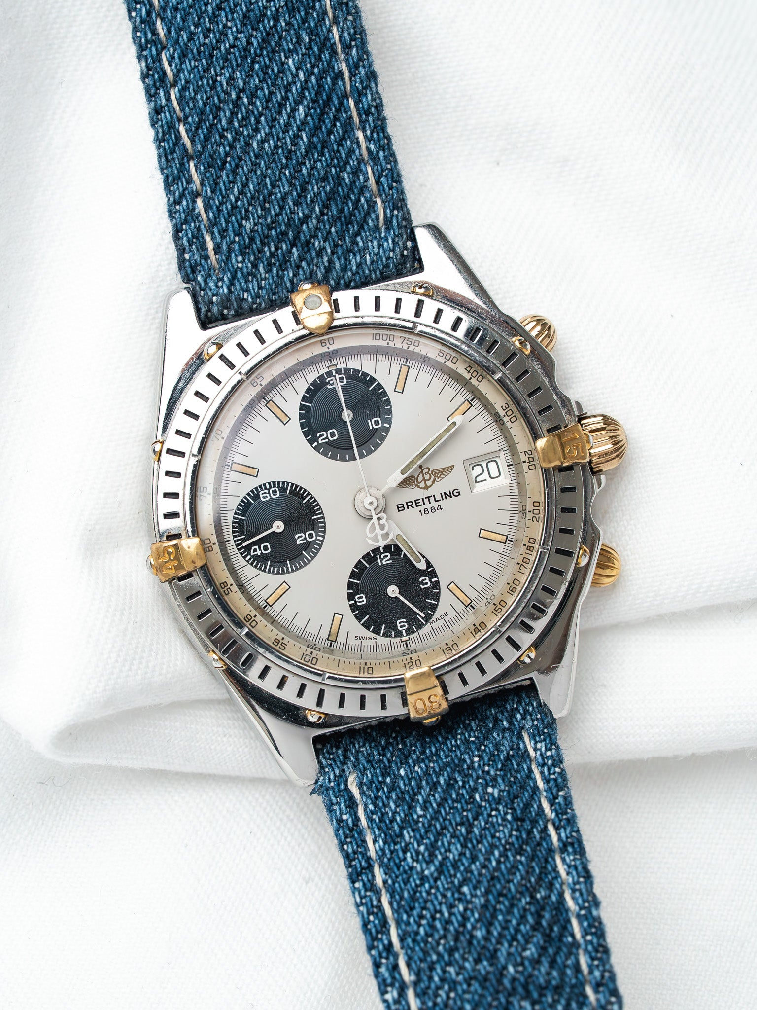 Breitling chronograph watch with silver dial, black subdials, and blue denim strap on white background