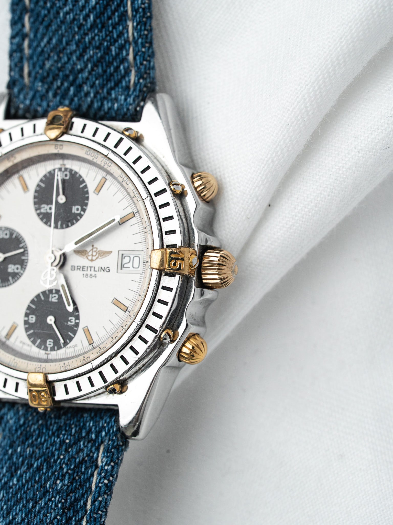 Breitling chronograph vintage with white dial, gold accents, denim strap on white fabric
