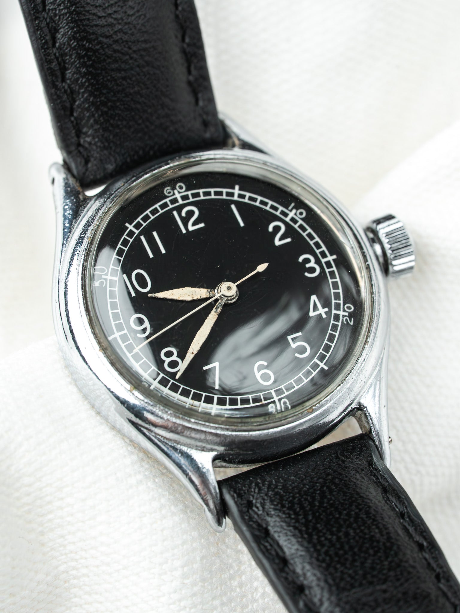Vintage watch with black dial, white numerals, steel case, and black leather strap