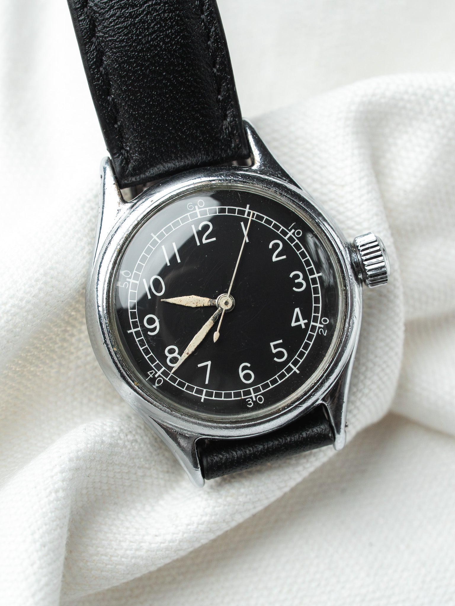 Vintage watch with black dial, white numerals, steel case, black leather strap on white fabric