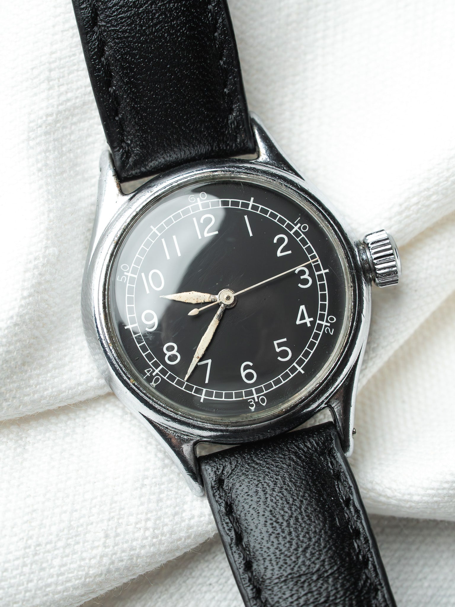 Vintage watch with black dial, white numerals, steel case, and black leather strap on white fabric