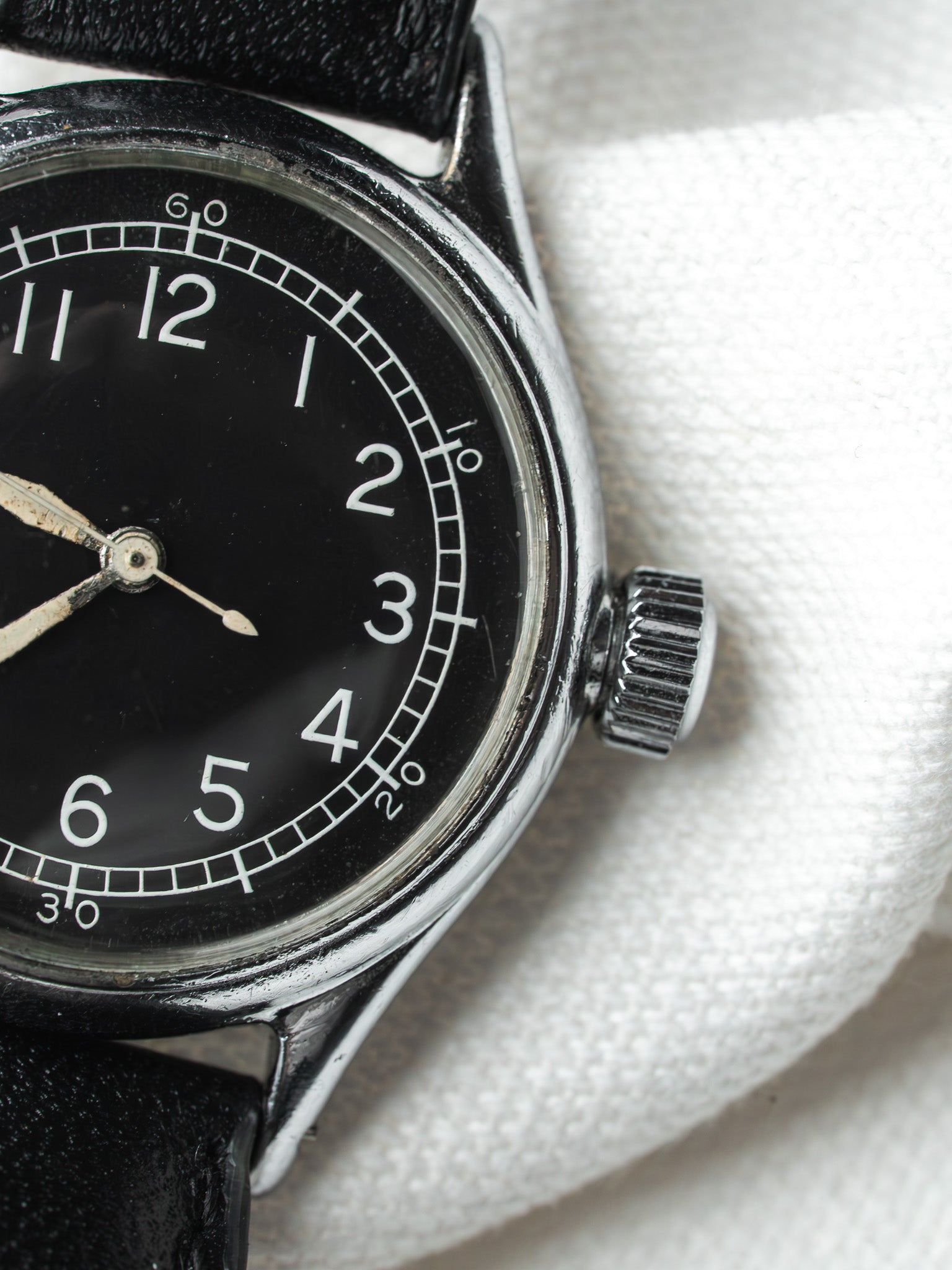 Vintage watch with black dial, white numerals, steel case, and black leather strap on white fabric