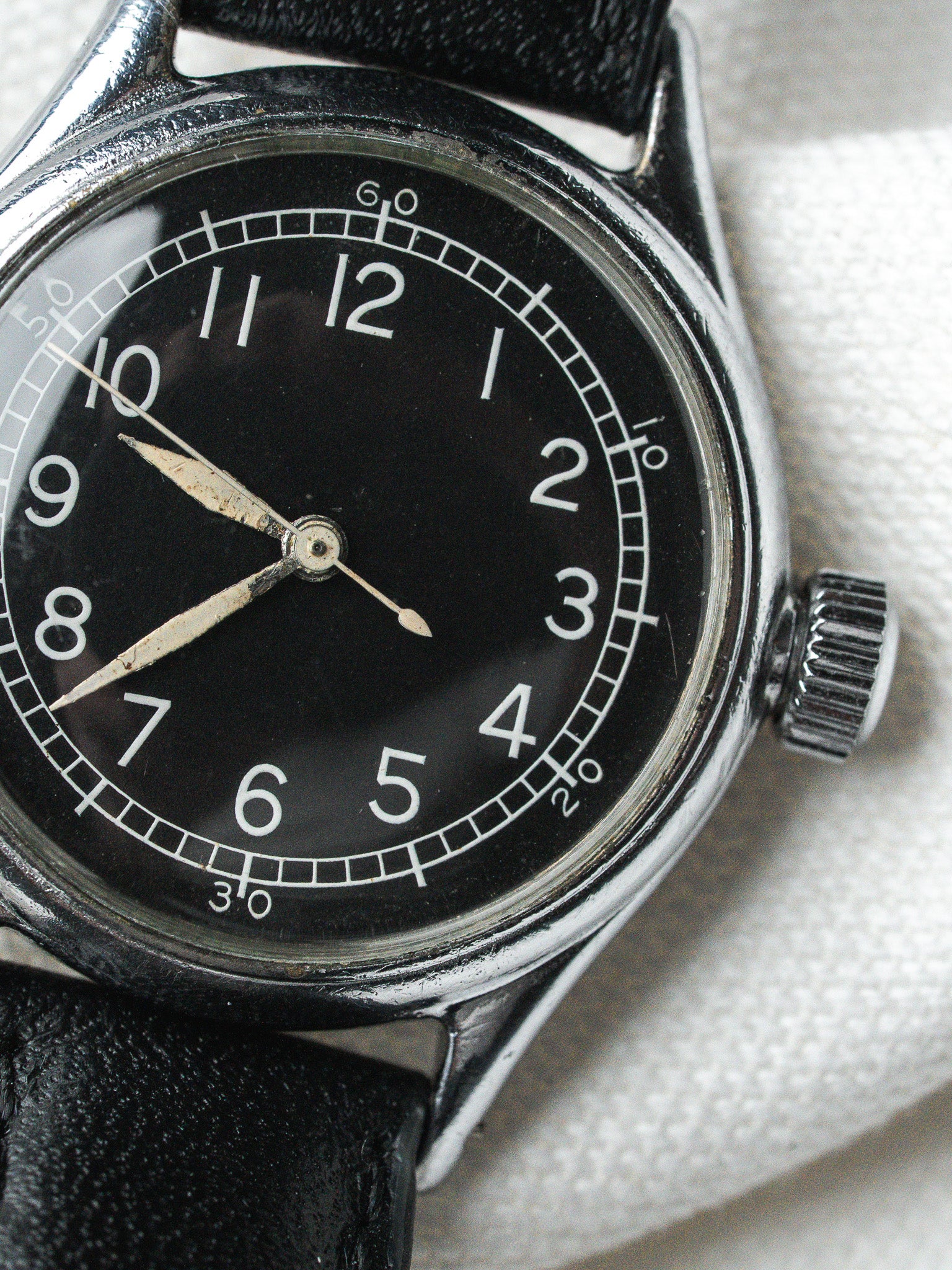 Vintage watch with black dial, white numerals, steel case, and black leather strap