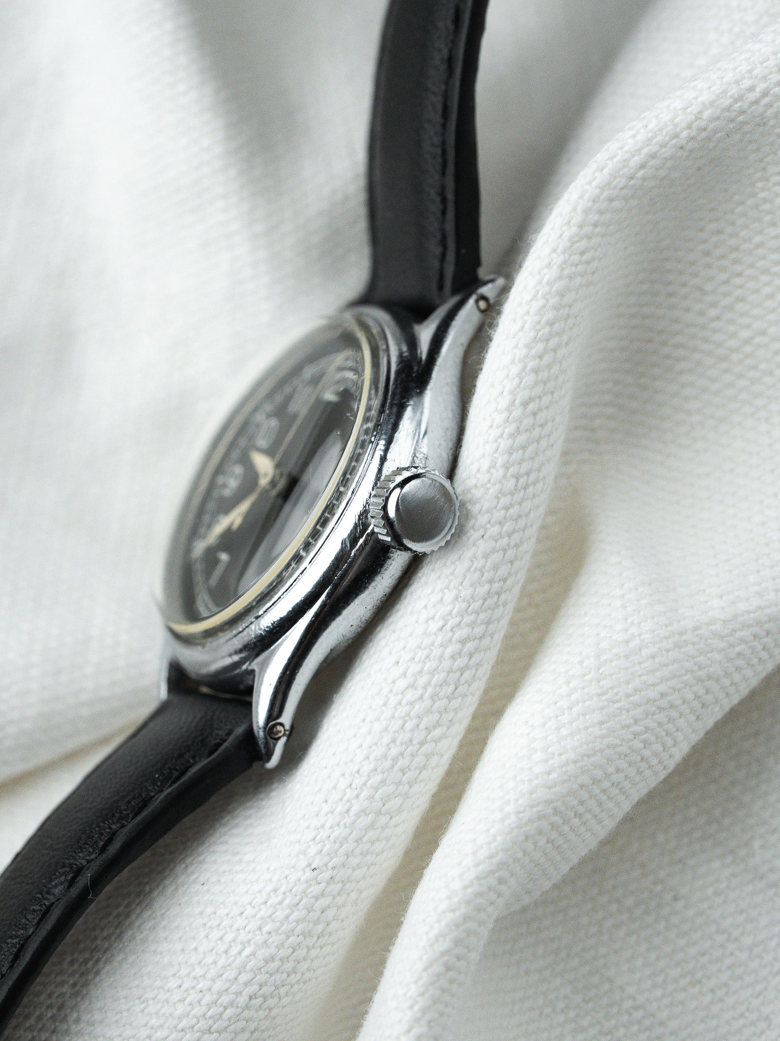 Vintage Omega watch with black dial, steel case, and black leather strap on white fabric
