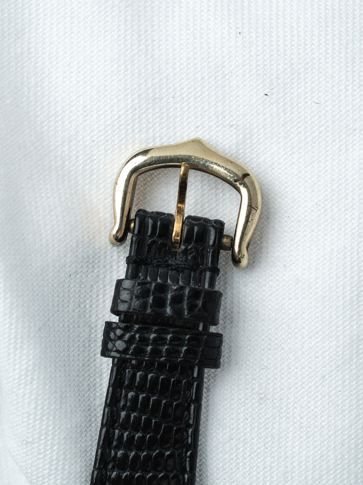 Black alligator leather watch strap with gold-tone buckle on white fabric