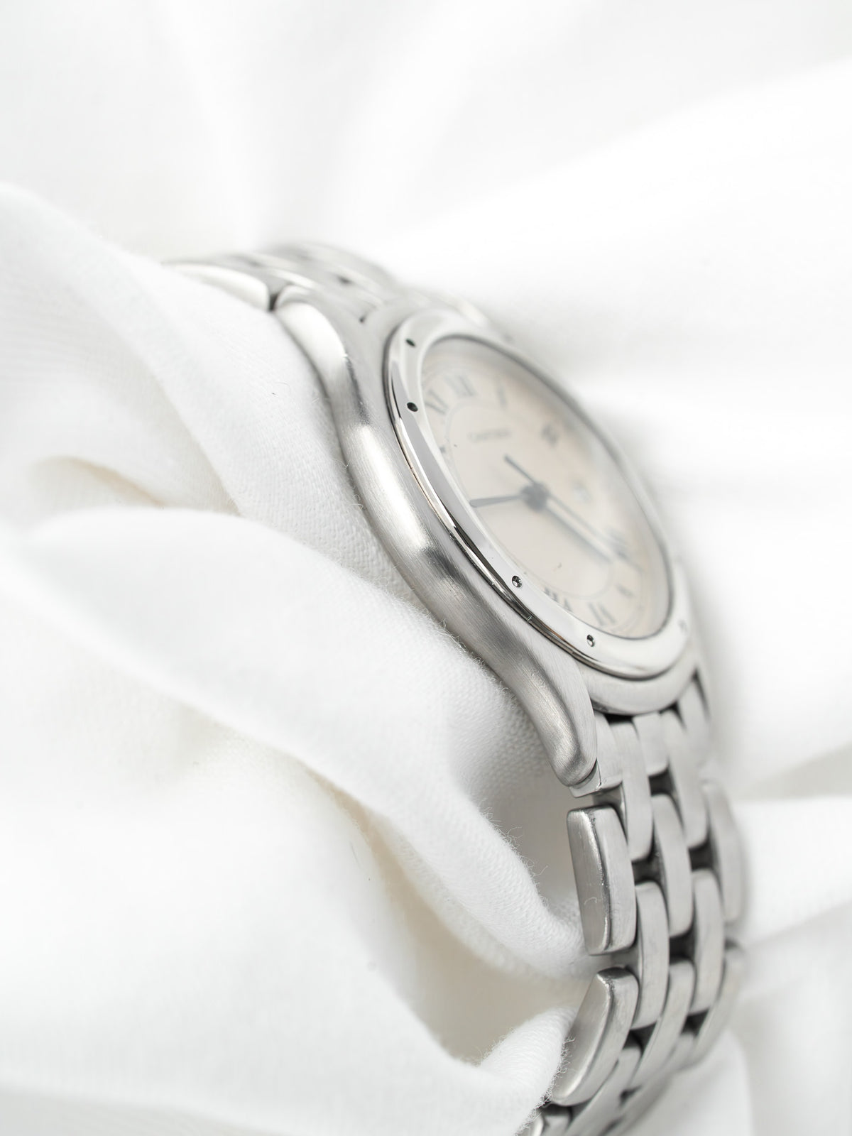 Montre Cartier vintage en acier, cadran blanc et bracelet métallique sur tissu blanc