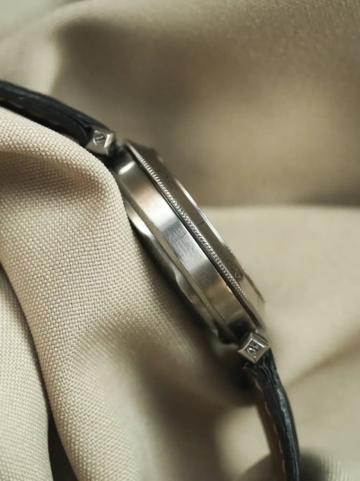 Omega vintage watch side view, stainless steel case, black leather strap on fabric