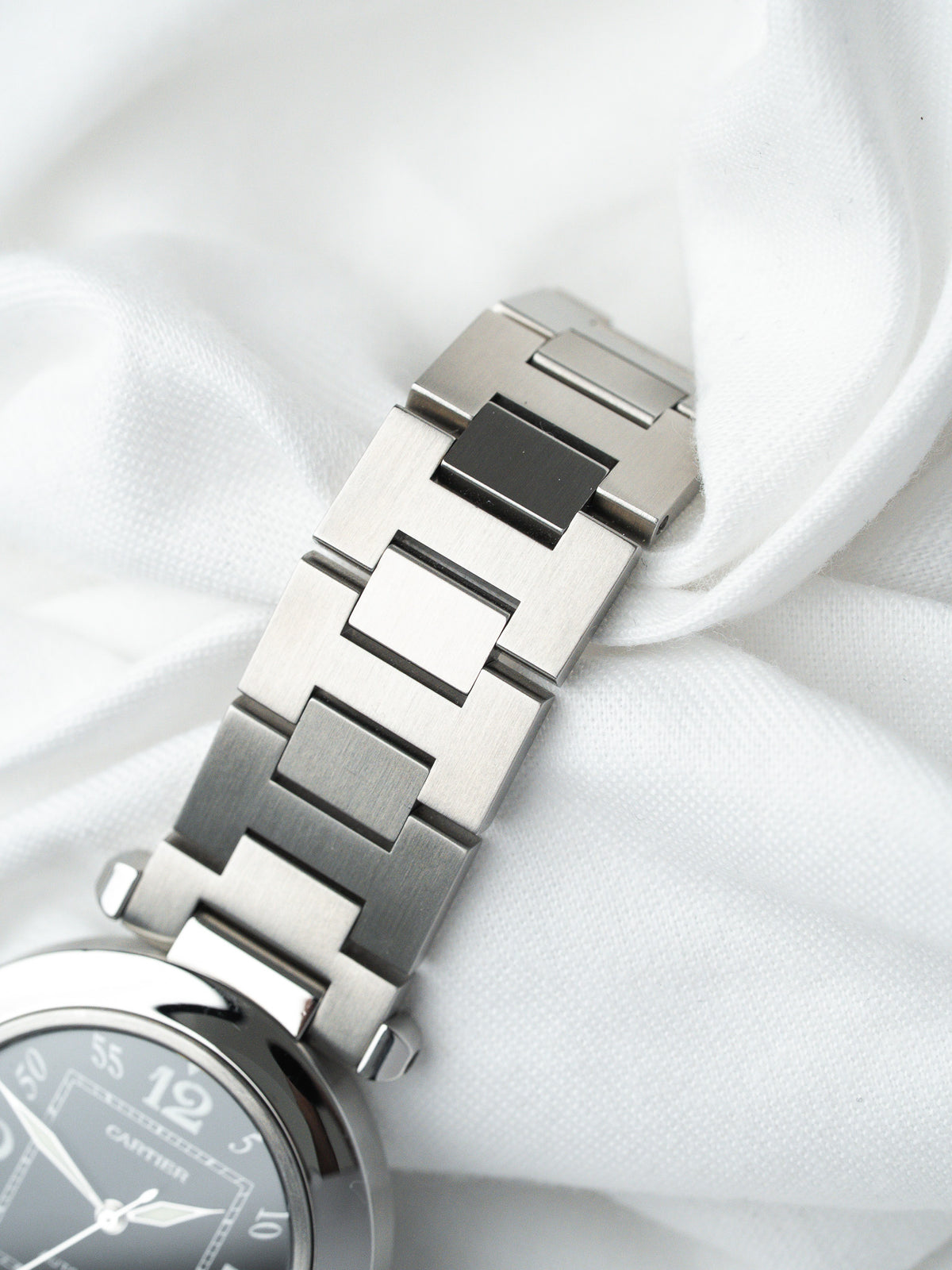 Cartier watch with steel bracelet, gray dial, and polished links on white fabric