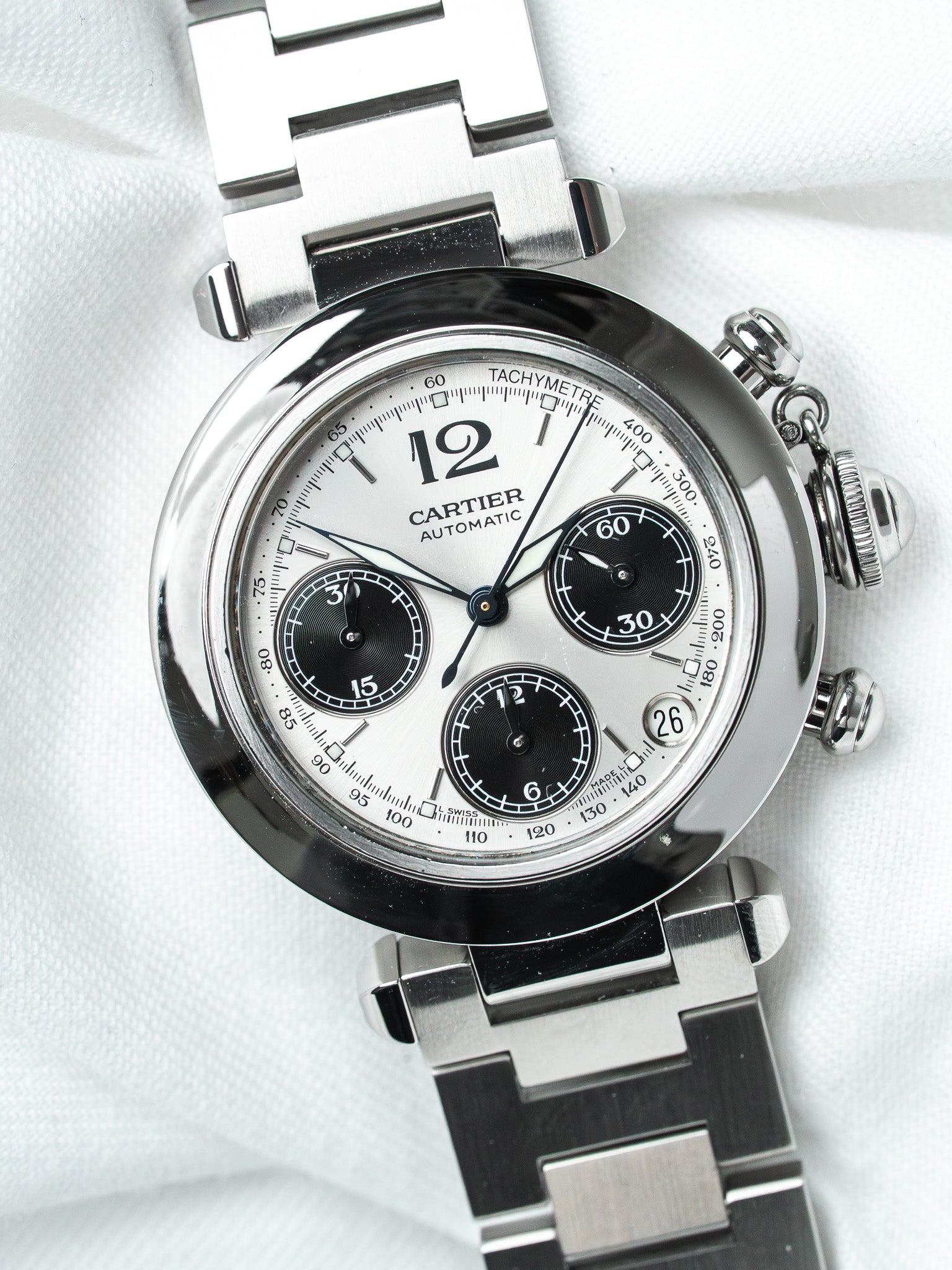 Cartier chronograph watch with silver dial, black subdials, and steel bracelet on white fabric