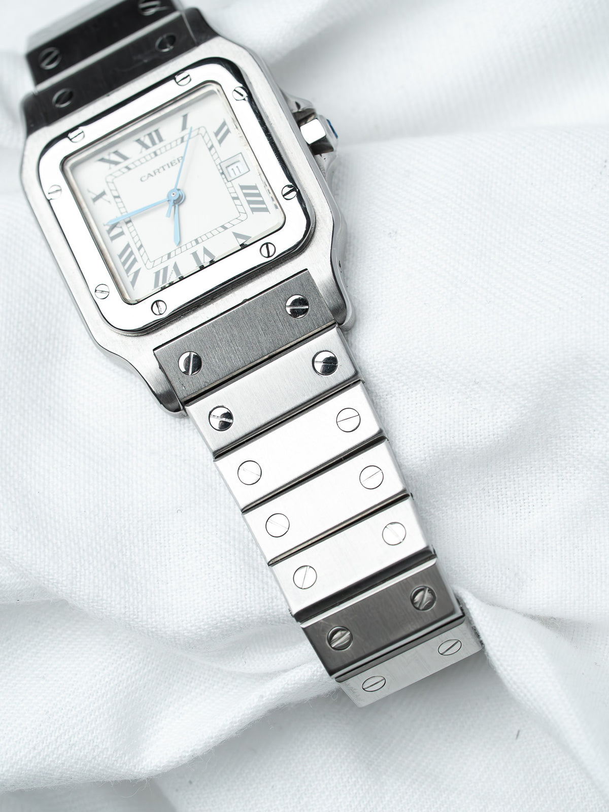 Cartier Santos watch with white dial, Roman numerals, and steel bracelet on white fabric