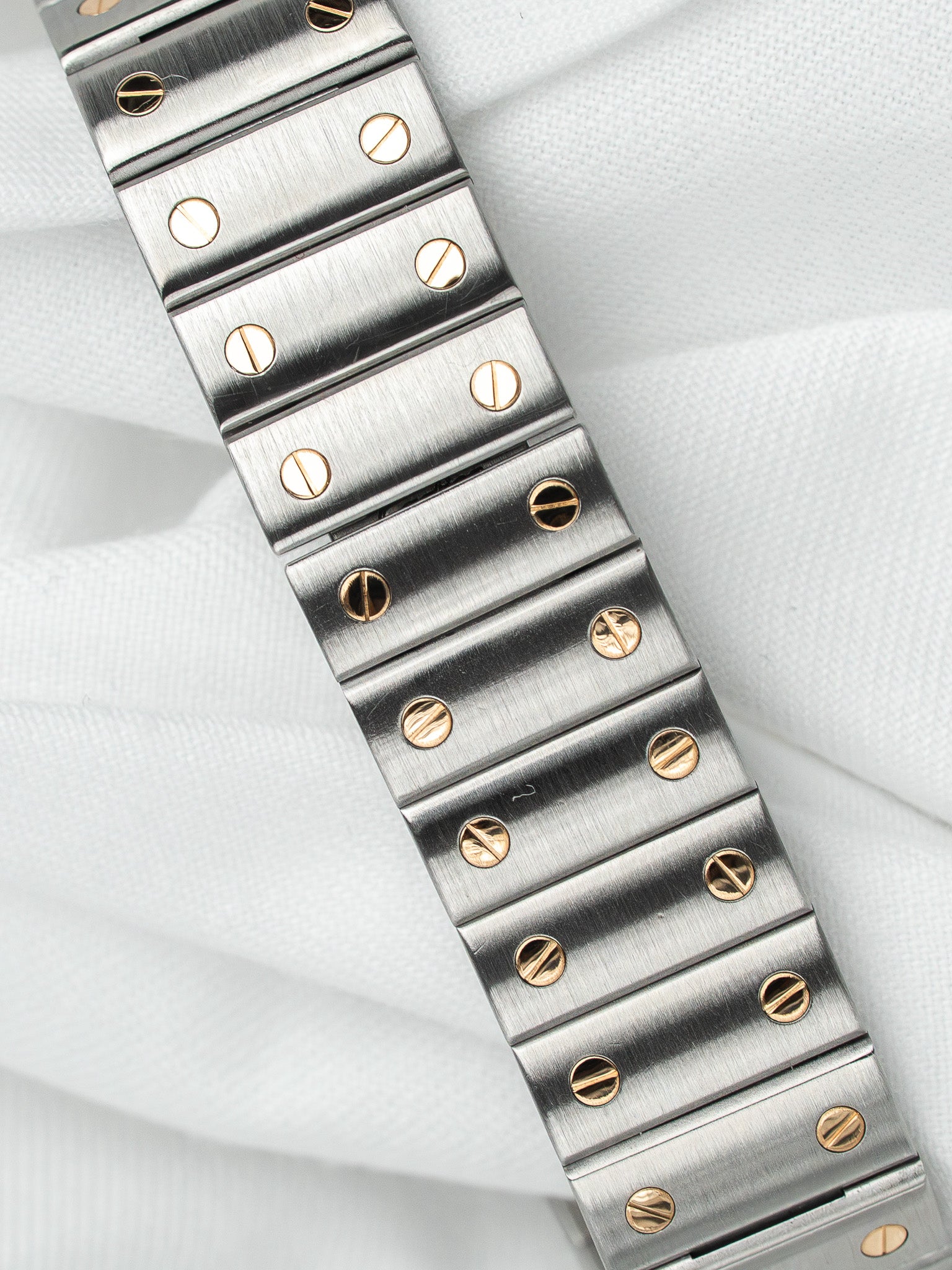 Cartier vintage bracelet with brushed steel links and gold screws on white fabric