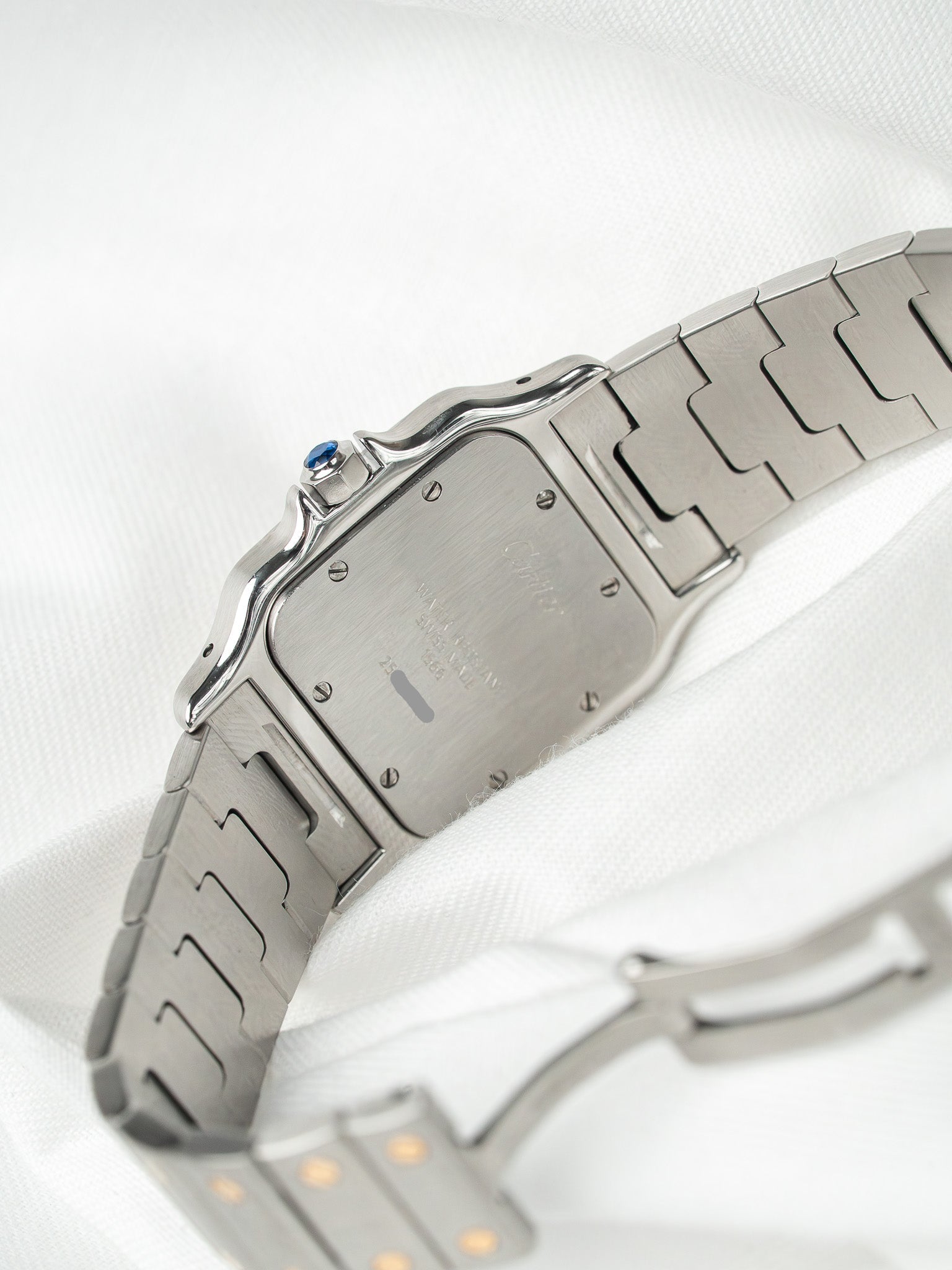 Cartier Santos watch with steel case, blue cabochon crown, and integrated bracelet on white fabric