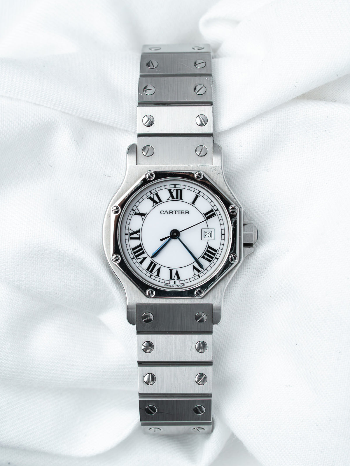 Cartier Santos watch with white dial, Roman numerals, and steel bracelet on white fabric