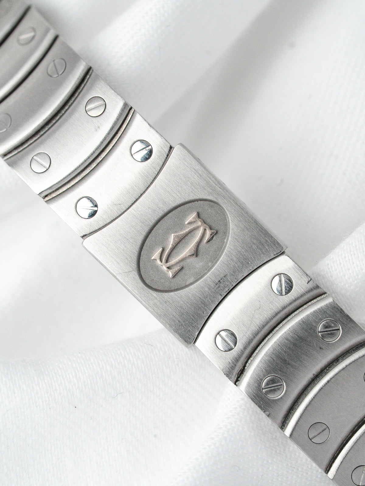 Cartier vintage watch bracelet with iconic logo, brushed steel links, and screw details on white fabric