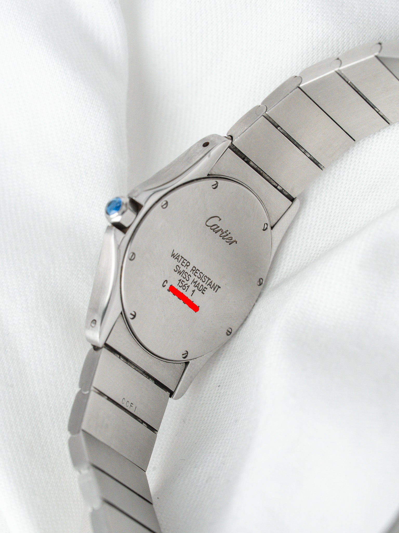 Cartier watch back with engraved logo, water resistant text, and blue crown on white fabric