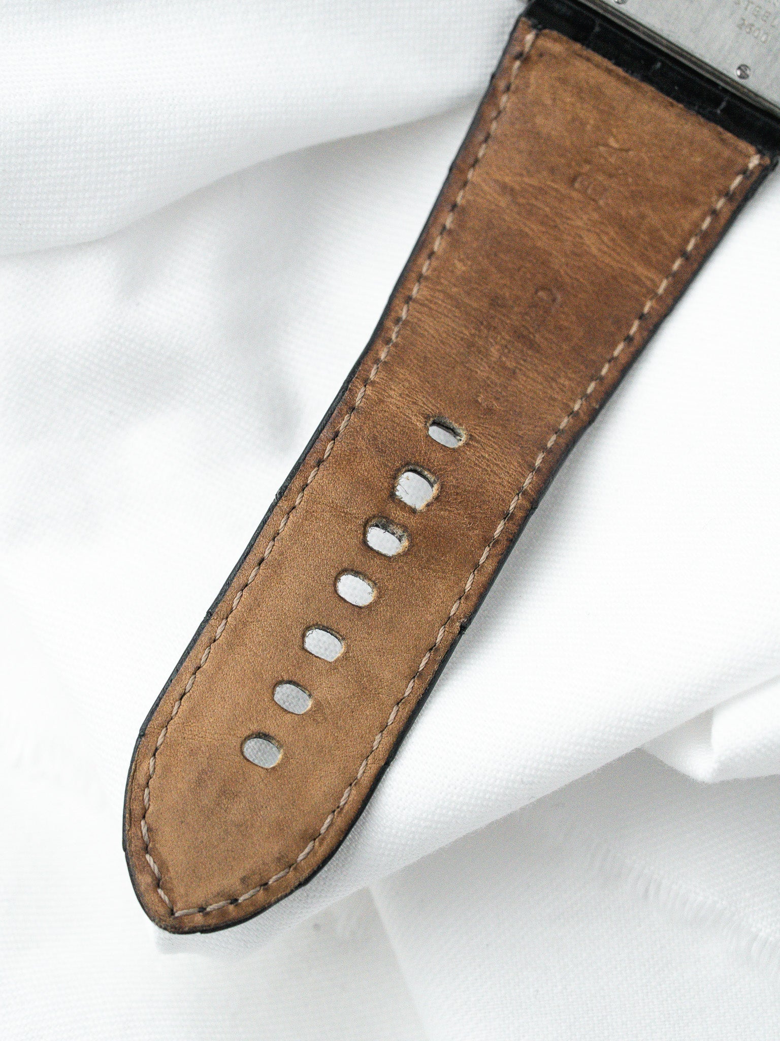 Vintage watch strap in brown leather with white stitching, resting on white fabric