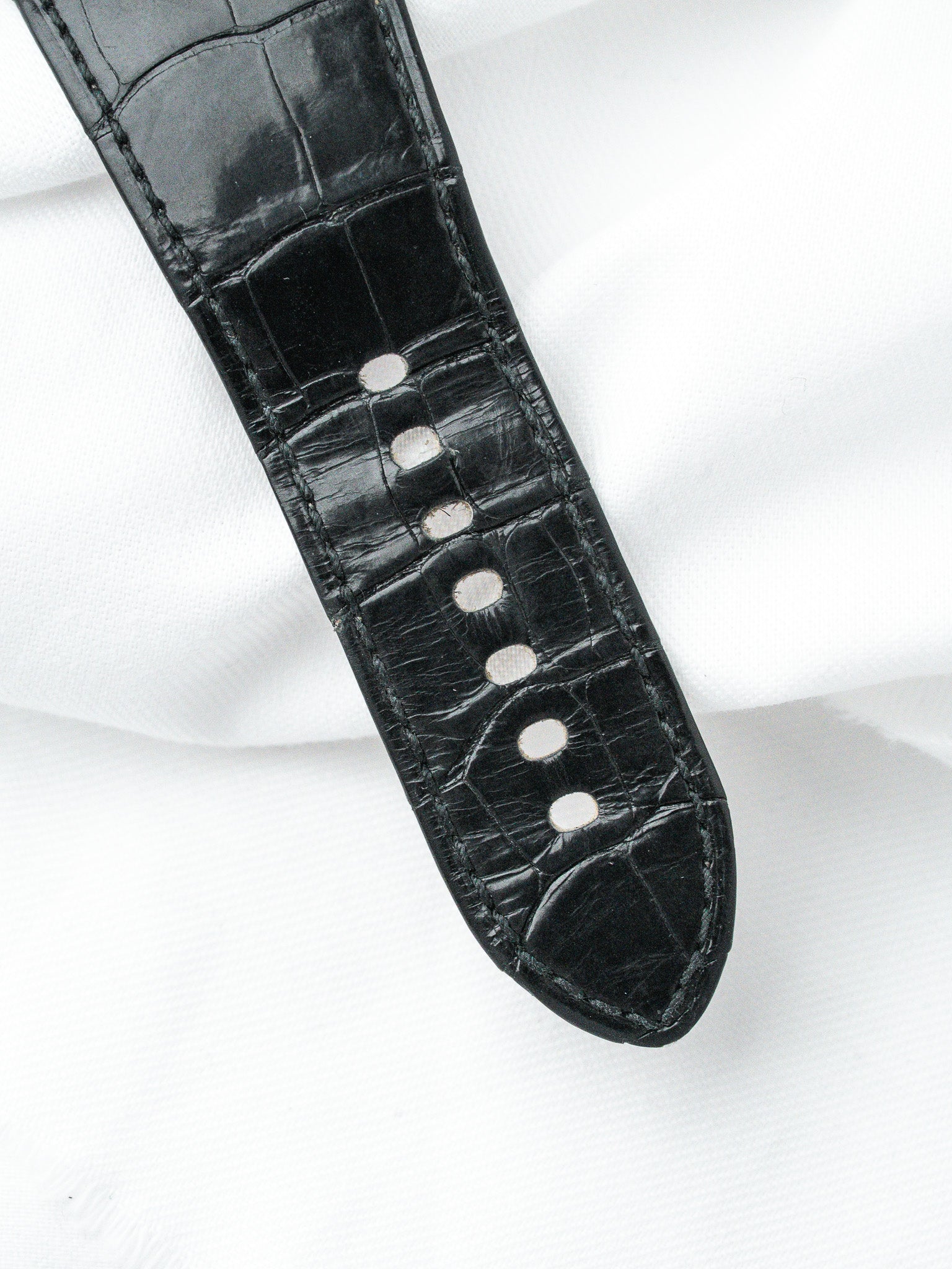 Black alligator leather watch strap with white stitching on white background
