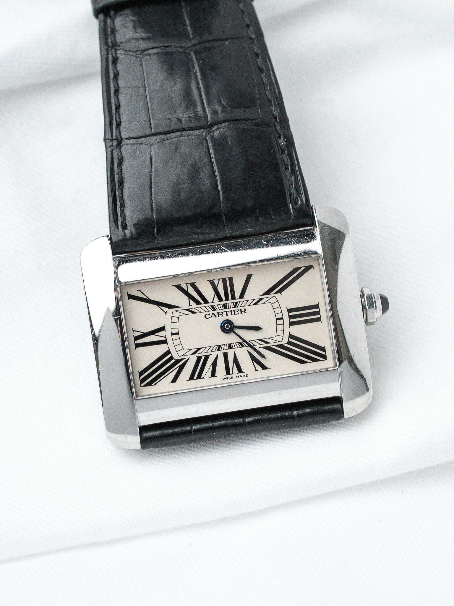 Cartier Tank watch with silver case, white dial, black Roman numerals, and black alligator strap