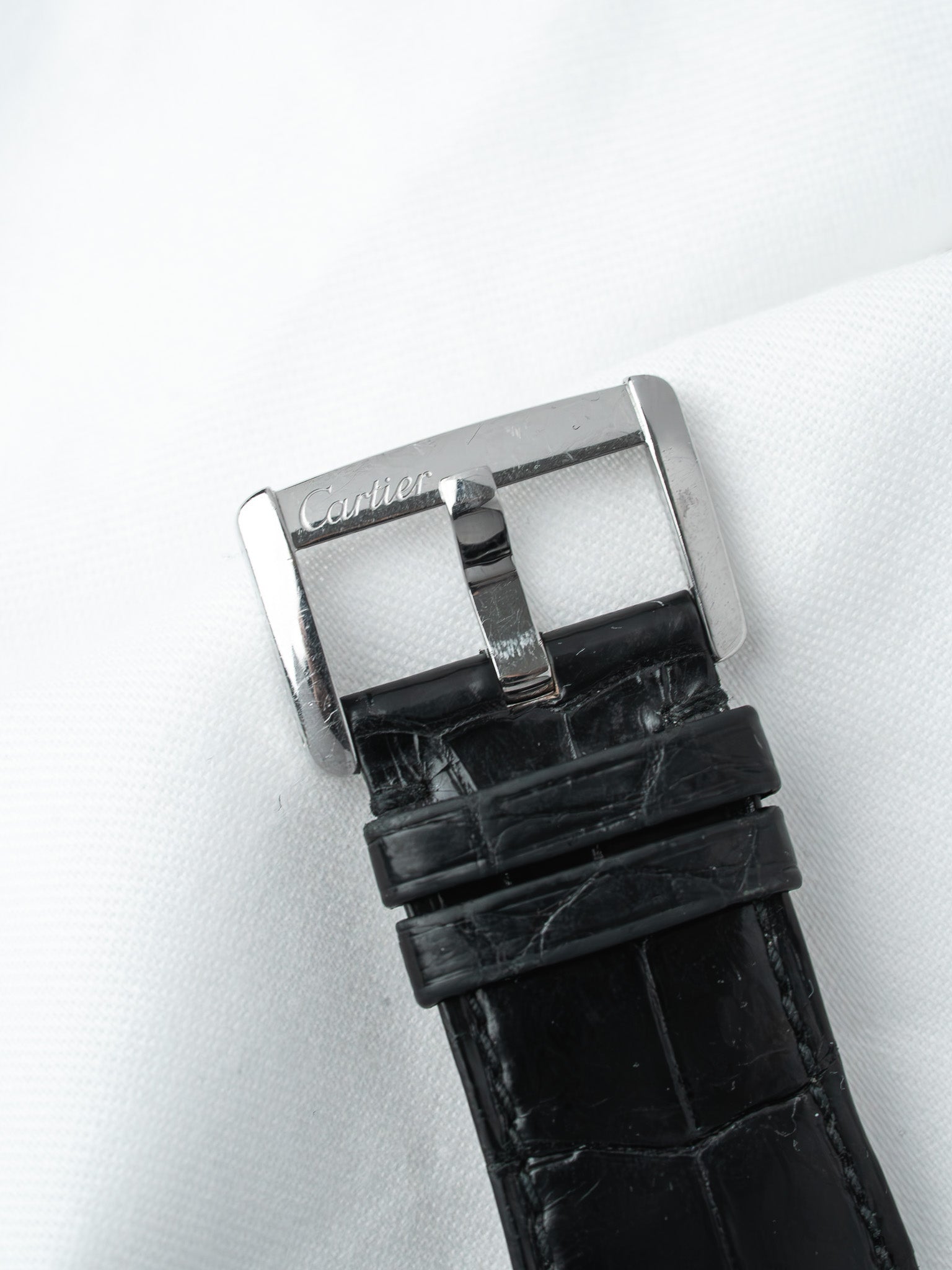 Cartier watch buckle with black alligator strap on white fabric background