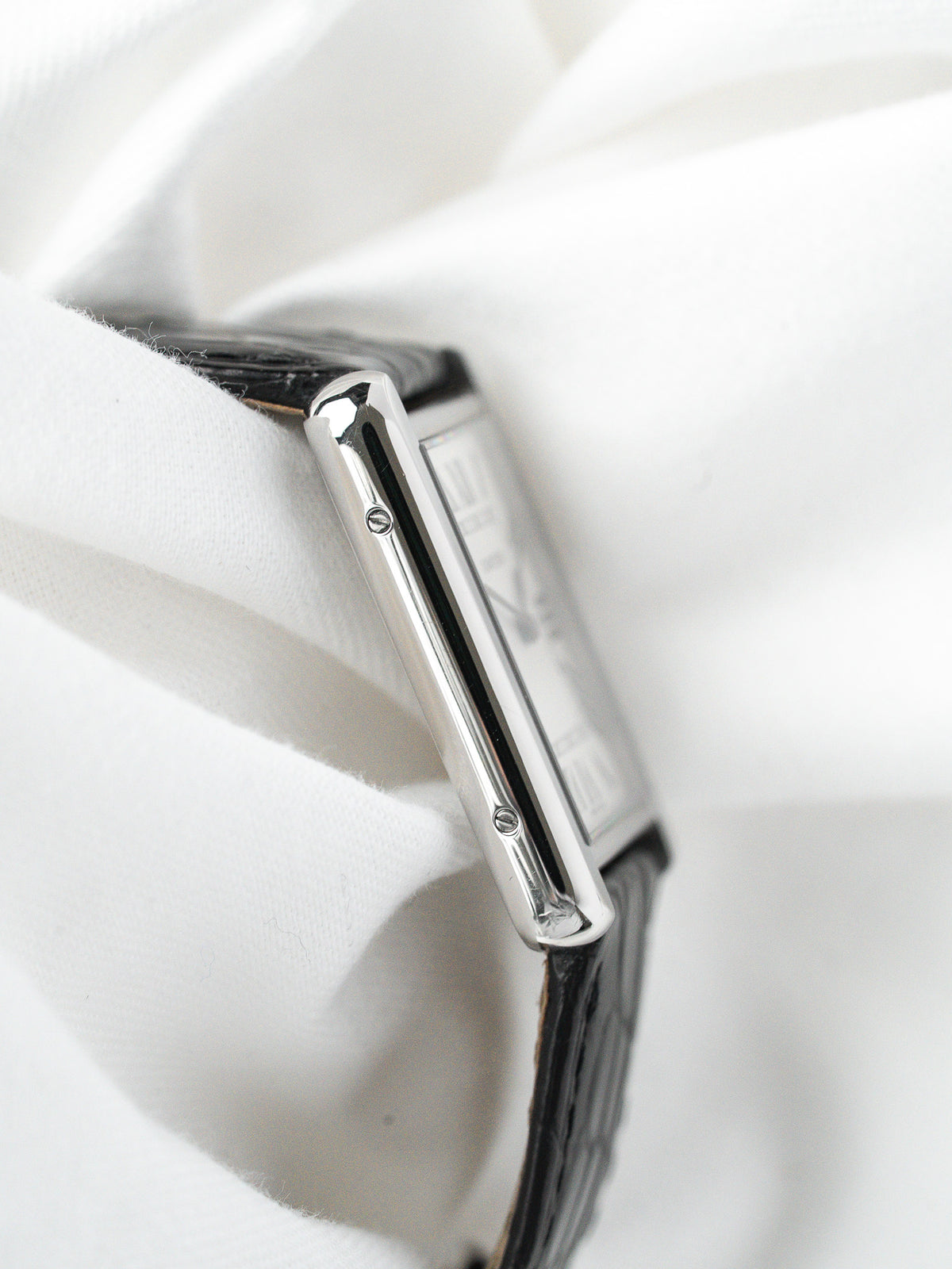 Montre Cartier Tank vintage, boîtier rectangulaire en acier, bracelet cuir noir sur fond blanc