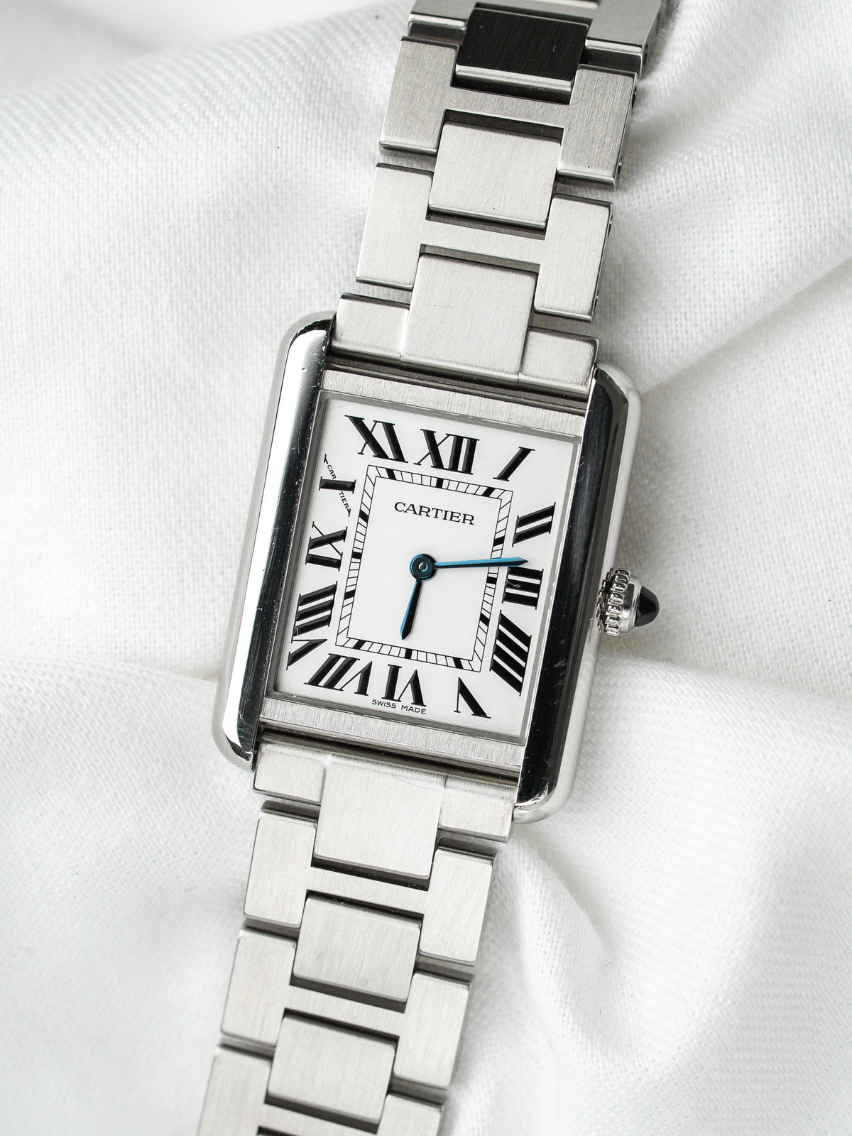 Montre Cartier Tank vintage en acier, boîtier rectangulaire et cadran blanc sur fond textile