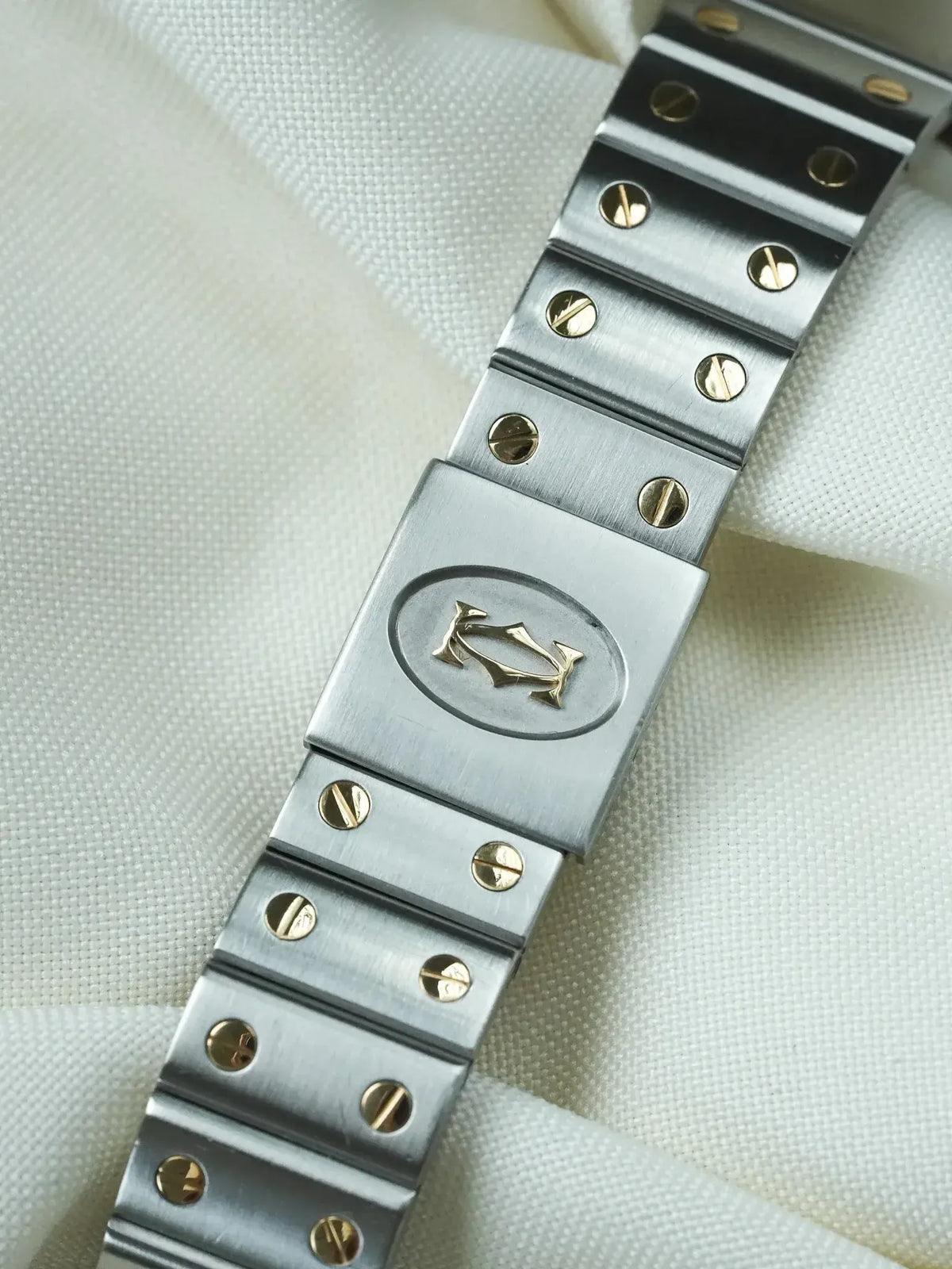 Cartier vintage watch bracelet with brushed steel links and gold screws on white fabric