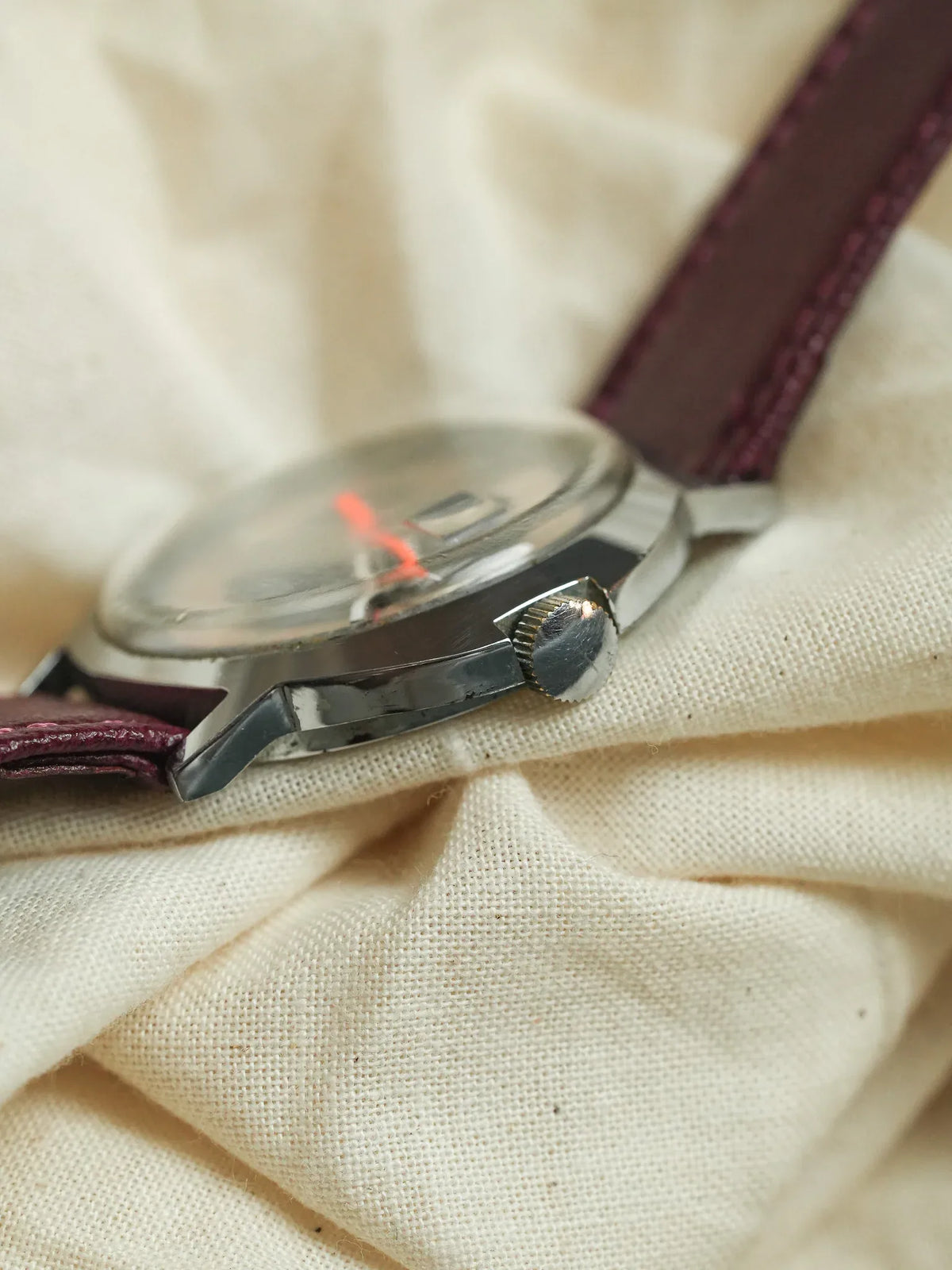 Vintage watch with stainless steel case, burgundy leather strap, resting on cream fabric