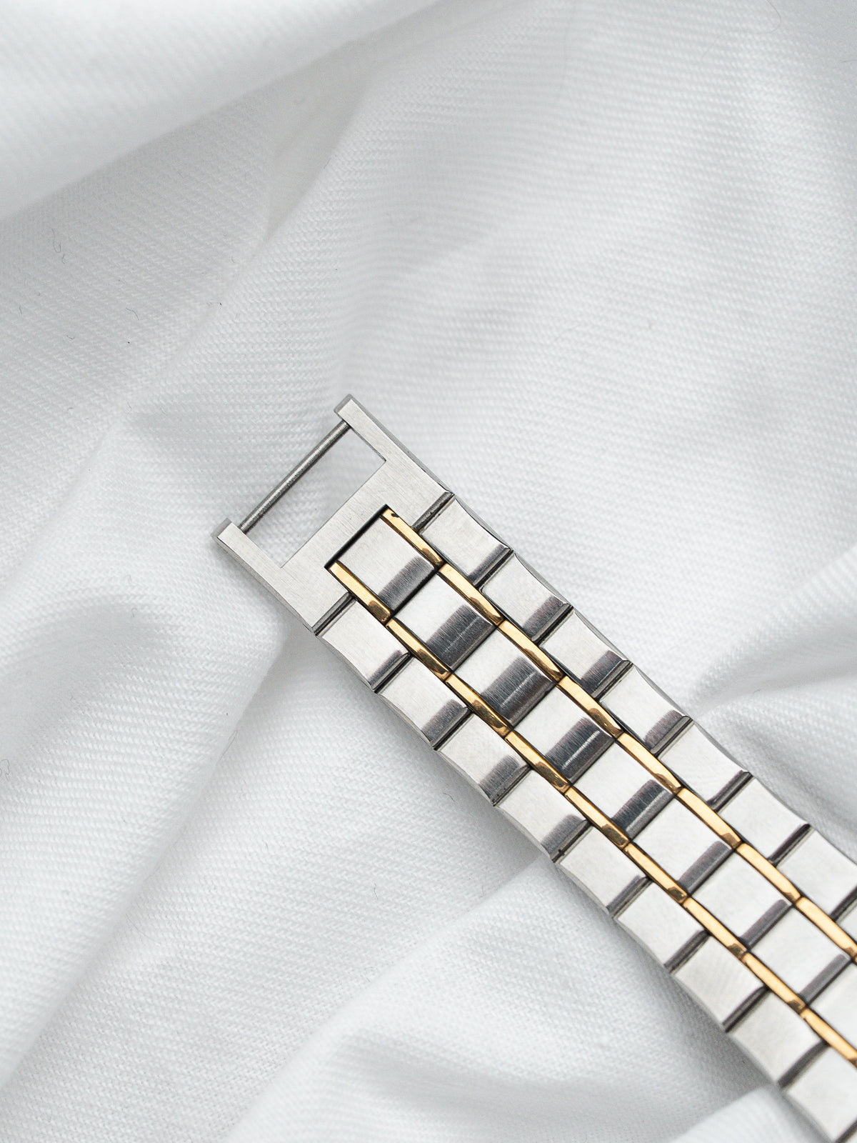 Bracelet de montre bicolore en acier et or posé sur un tissu blanc.
