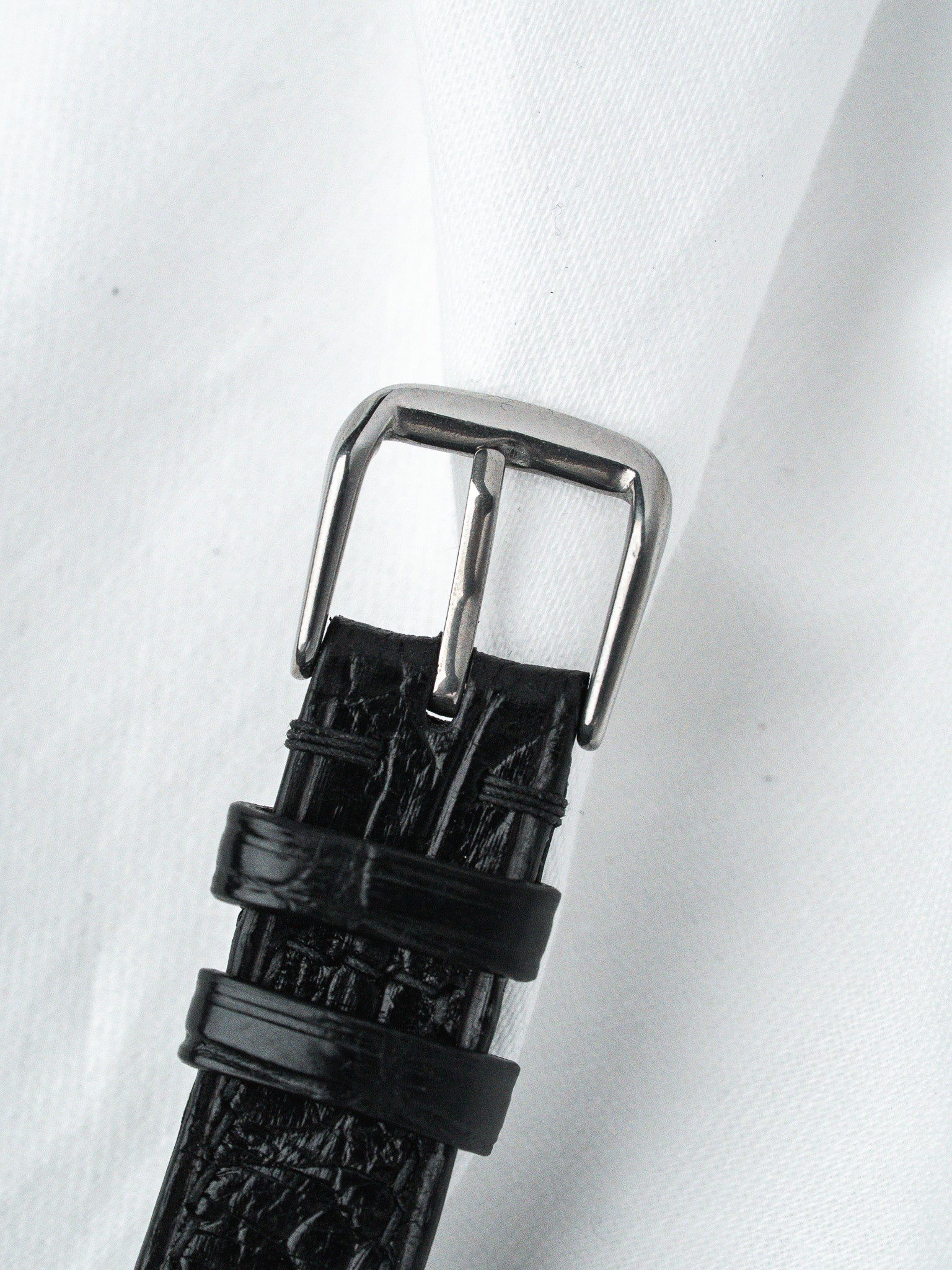 Black alligator leather watch strap with polished steel buckle on white fabric