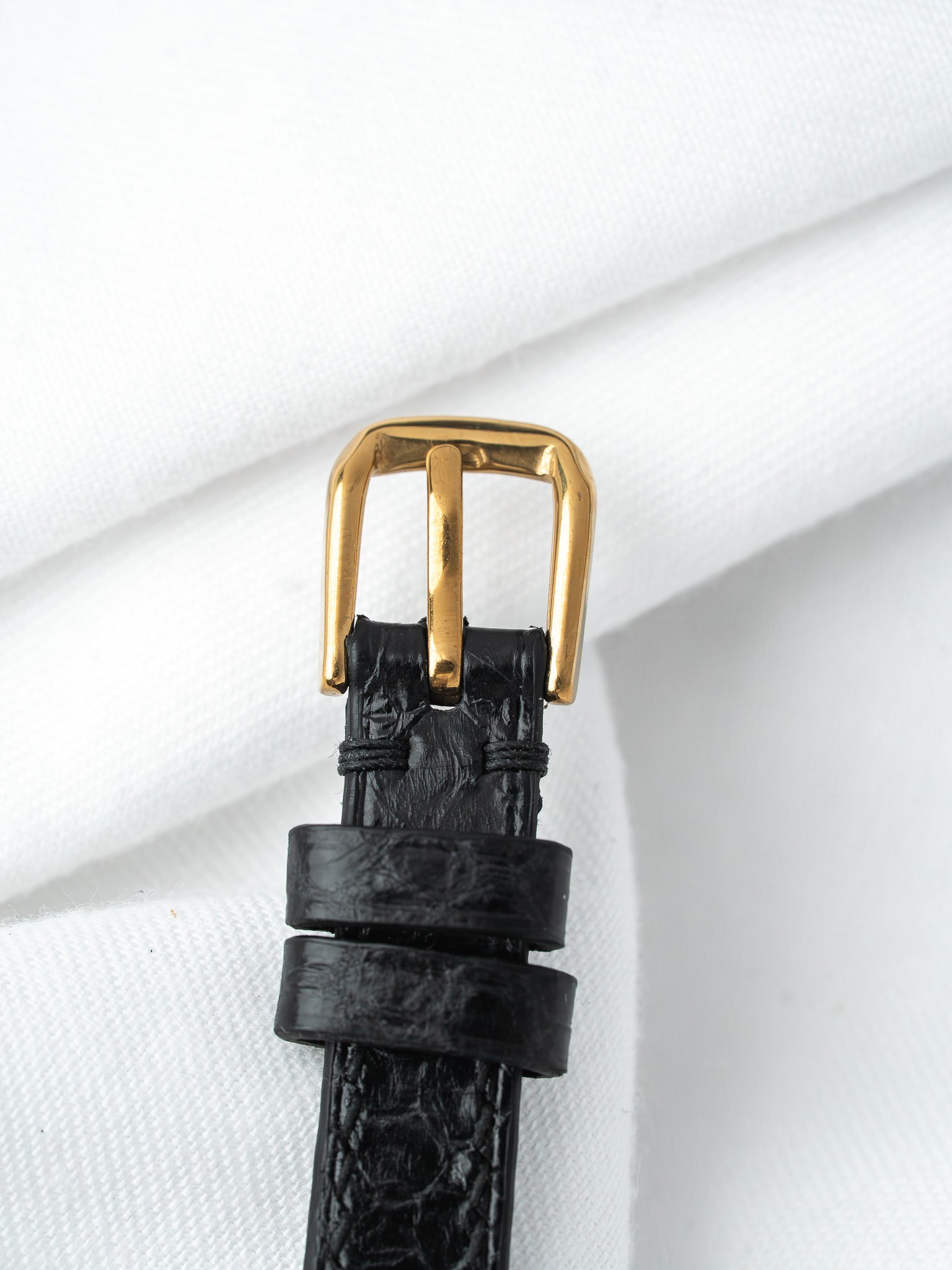 Black alligator leather watch strap with gold buckle on white fabric
