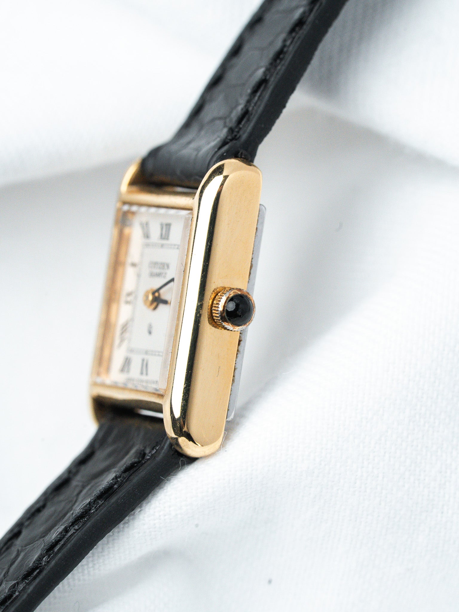 Citizen quartz vintage watch with gold case, white dial, black leather strap on white background