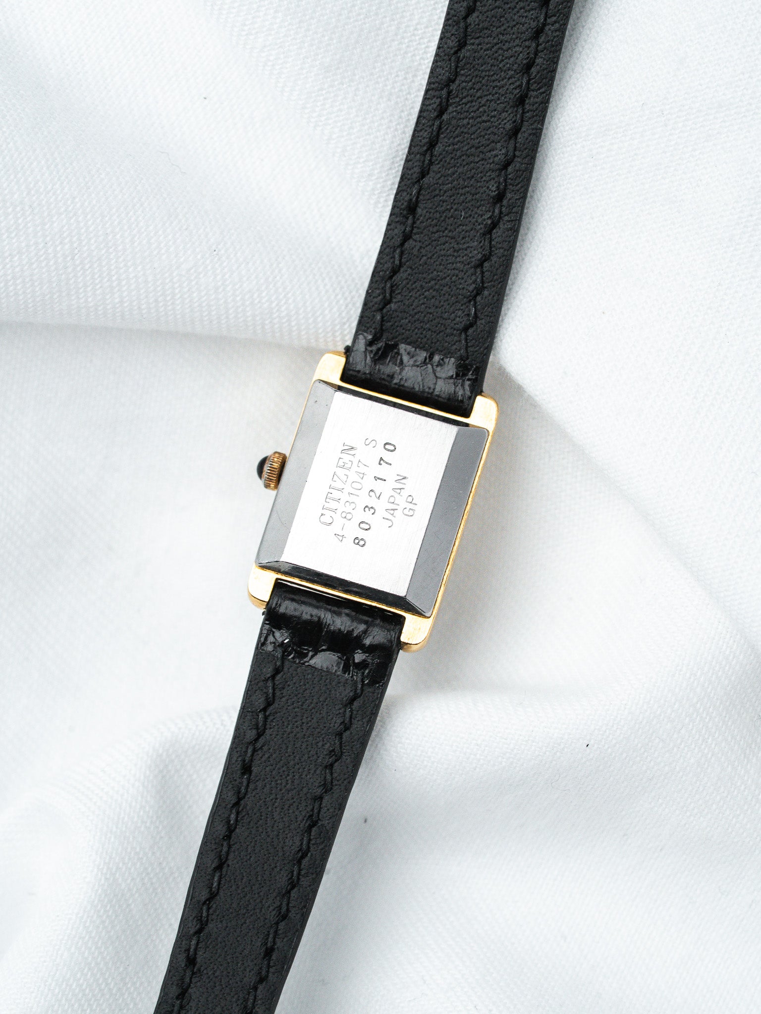 Citizen vintage watch with gold-tone case, black leather strap, and engraved back on white fabric