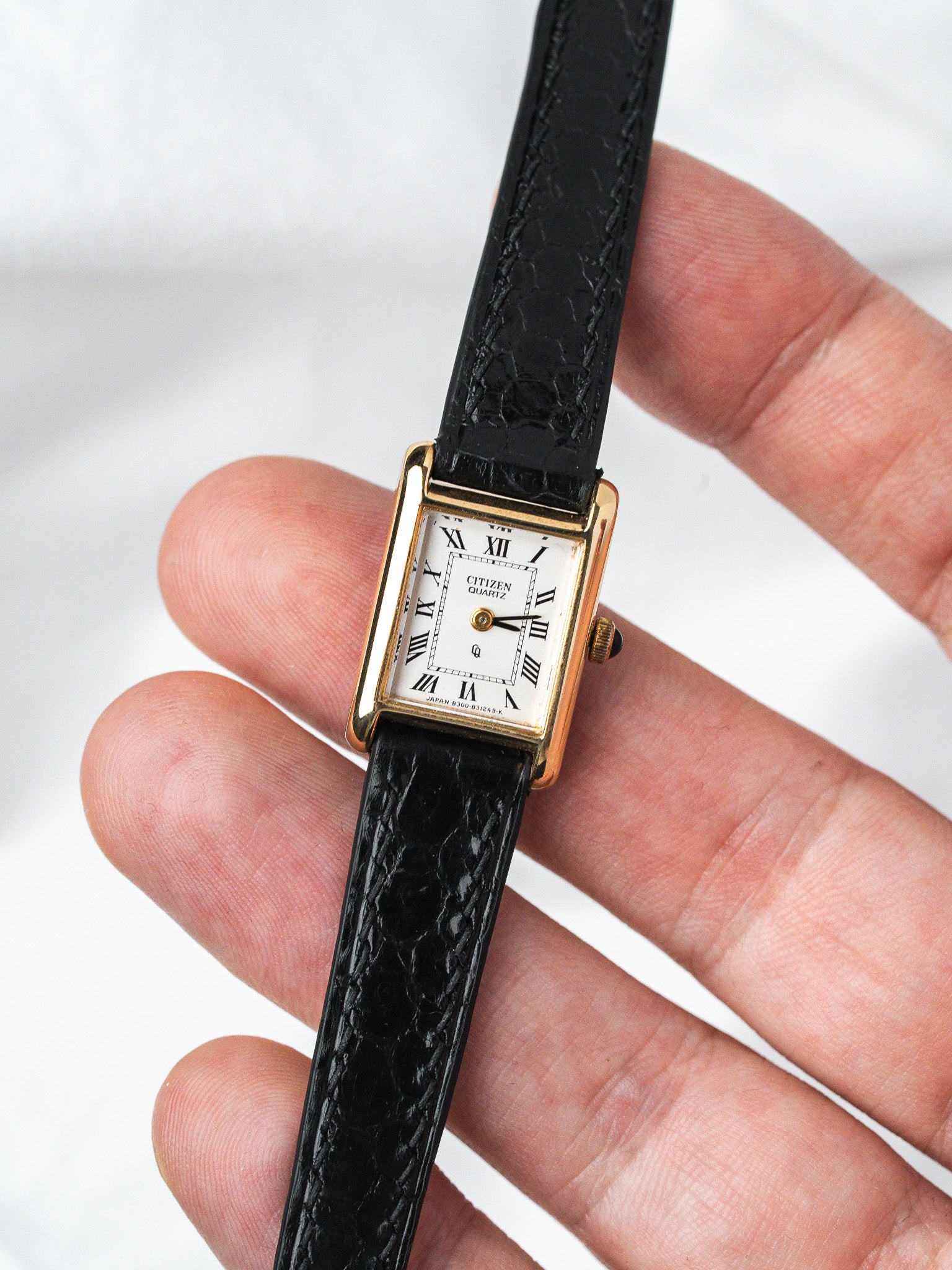 Citizen Quartz vintage watch with gold case, white dial, Roman numerals, black leather strap held in hand