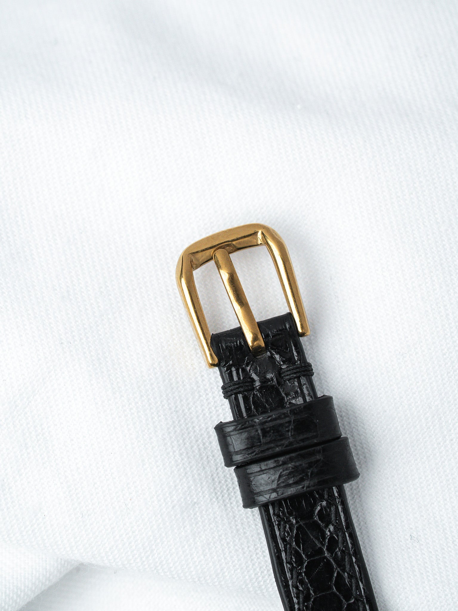 Black alligator leather watch strap with gold buckle on white fabric