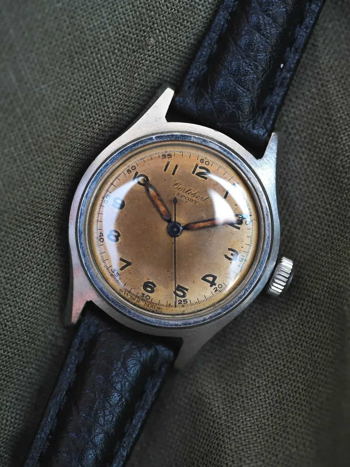 Vintage Cortébert Sport watch with cream dial, black leather strap, steel case on fabric